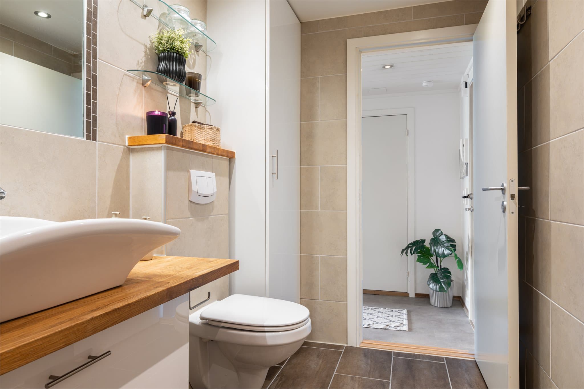 Rommet kombinerer bad og vaskerom med dusjhjørne i glass, vegghengt toalett og moderne innredning med servant på benkeplate.