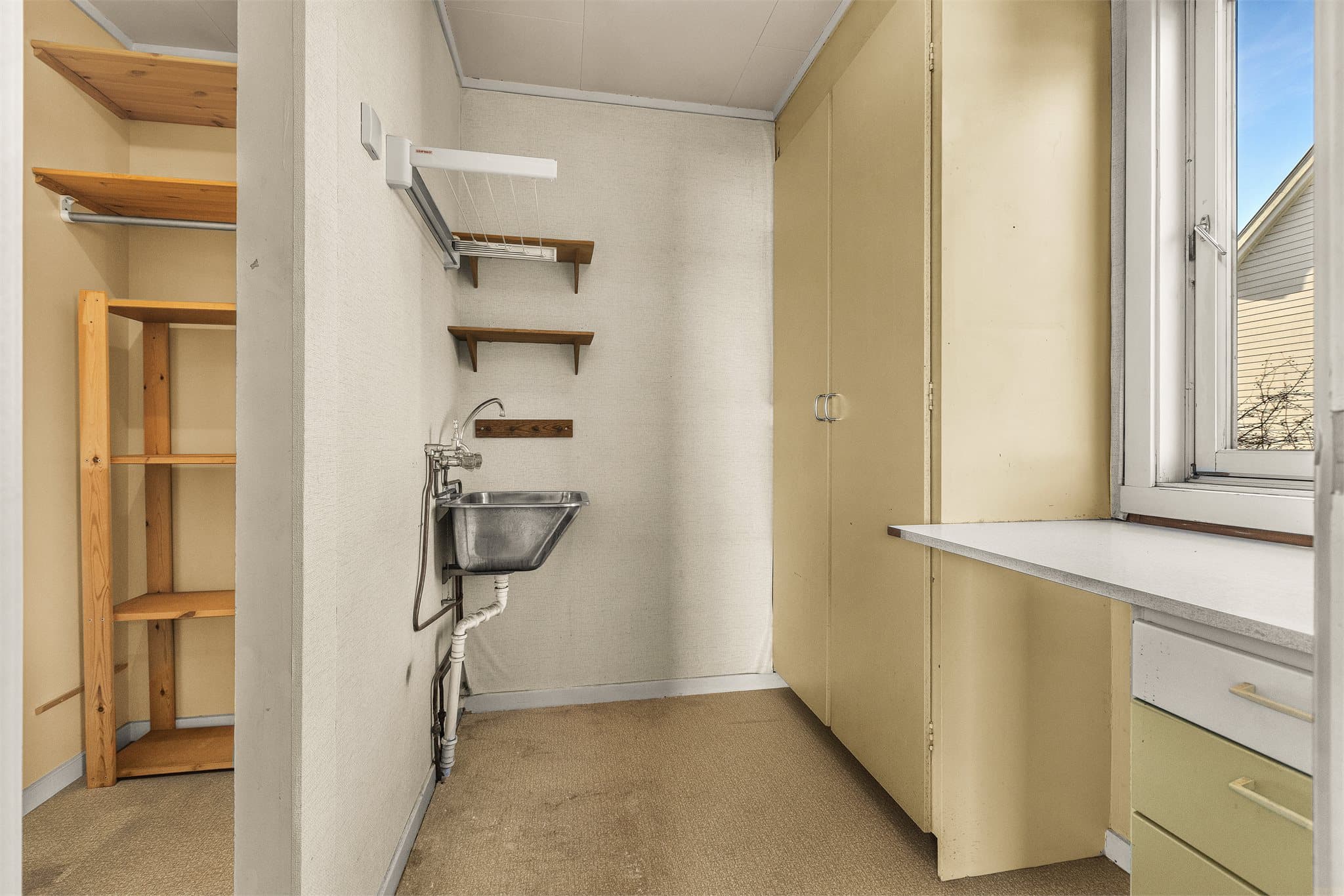 Kombinert vaskerom og bod med utslagsvask i stål og opplegg for vaskemaskin.