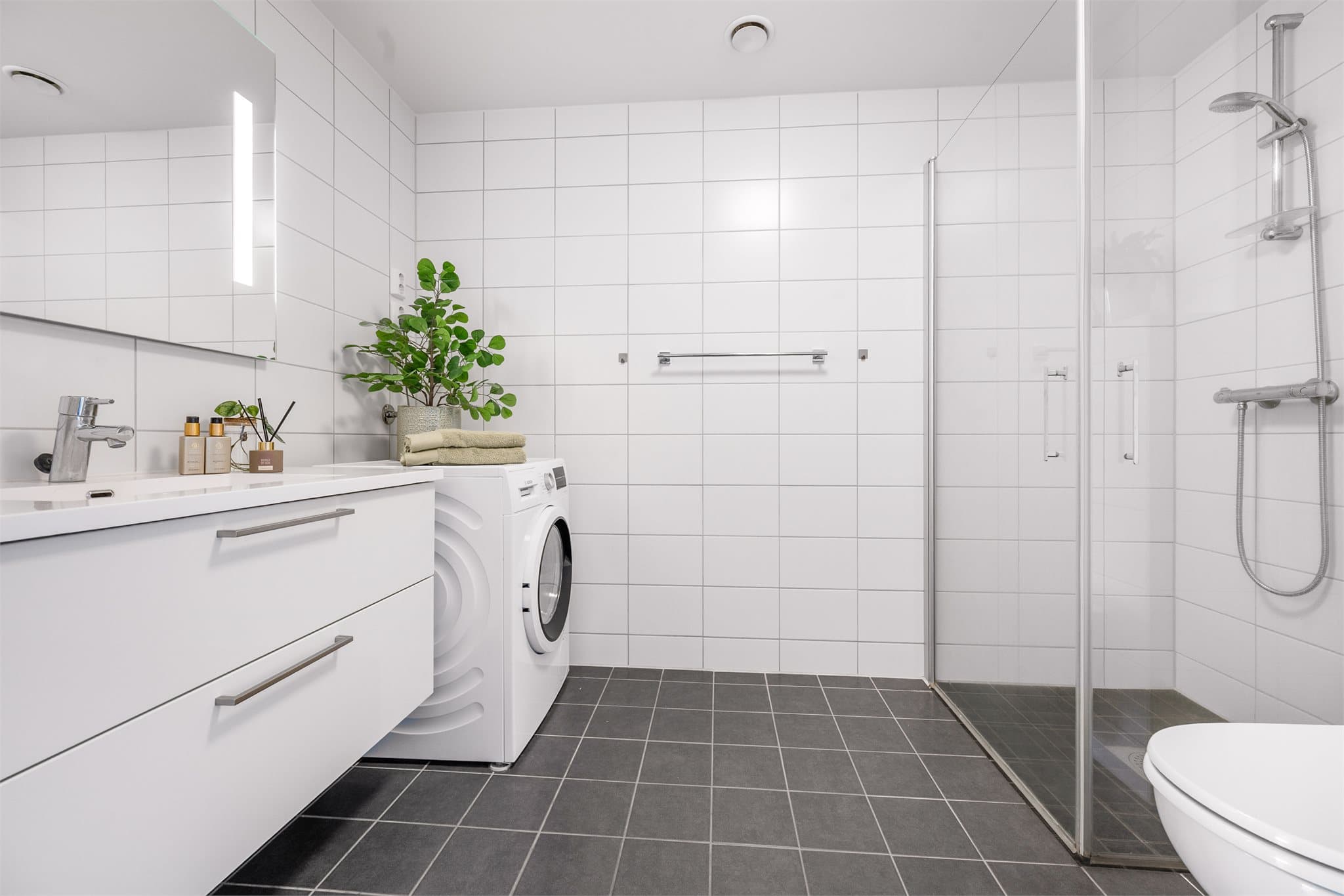 Pent og moderne baderom med stilren helservant på skuffeinnredning, vegghengt wc og praktisk dusjhjørne. Et lyst og innbydende rom som kombinerer funksjonalitet og et tidløst uttrykk.