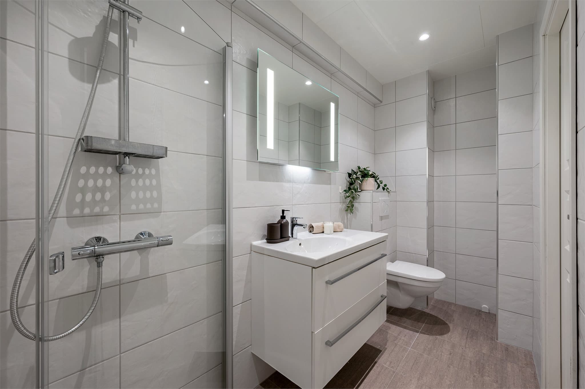 - Badet er innredet med vegghengt toalett, heldekkende servant, speil med belysning og dusjhjørne -