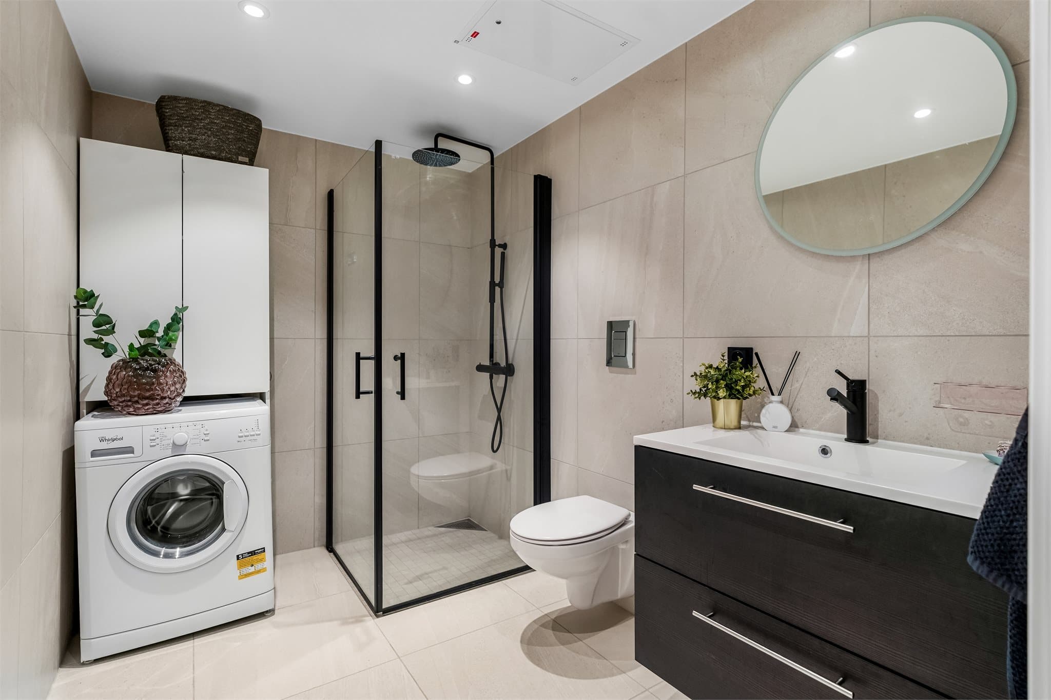 Badet har gulvvarme, downlights i taket og balansert ventilasjon. Innredningen består av servantskap med oppbevaring, speilskap, dusjhjørne med sorte detaljer, vegghengt toalett og opplegg for vaskemaskin.