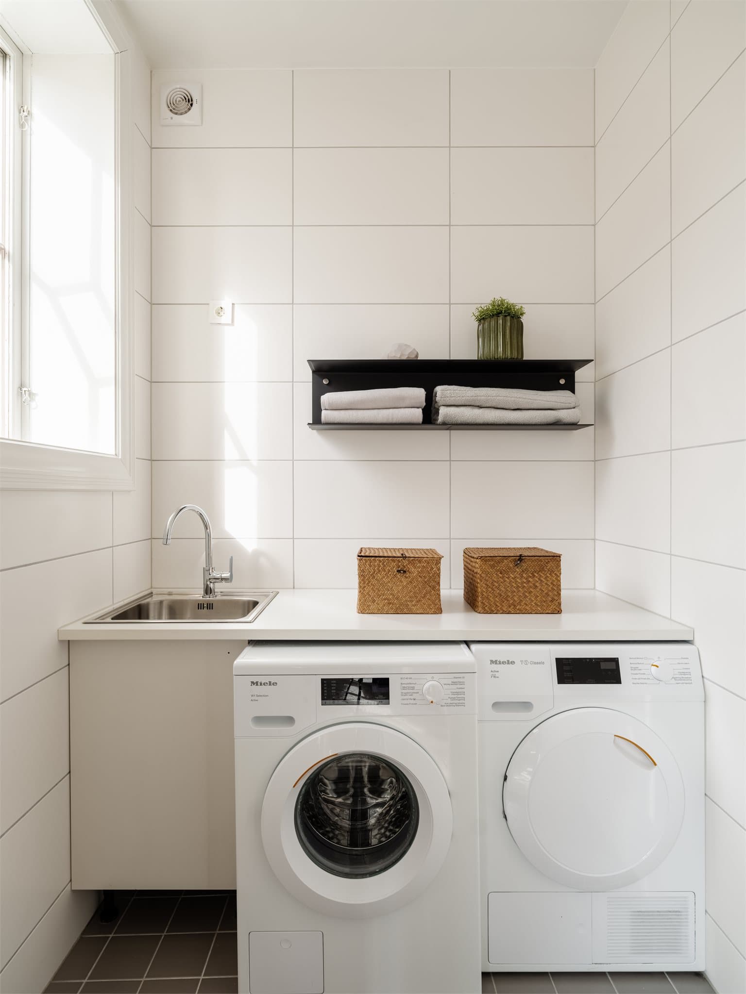 Fra kjøkkenet har man inngang til boligens praktiske vaskerom. Rommet har elektrisk gulvvarme, innfelt downlights og er innredet med vaskekum. Her er det også opplegg for vaskemaskin.