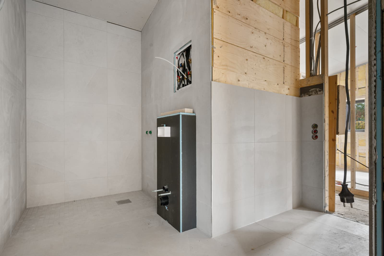 Påbegynt baderom nr. 2 med store fliser på vegg og gulv, tilrettelagt for vegghengt wc.