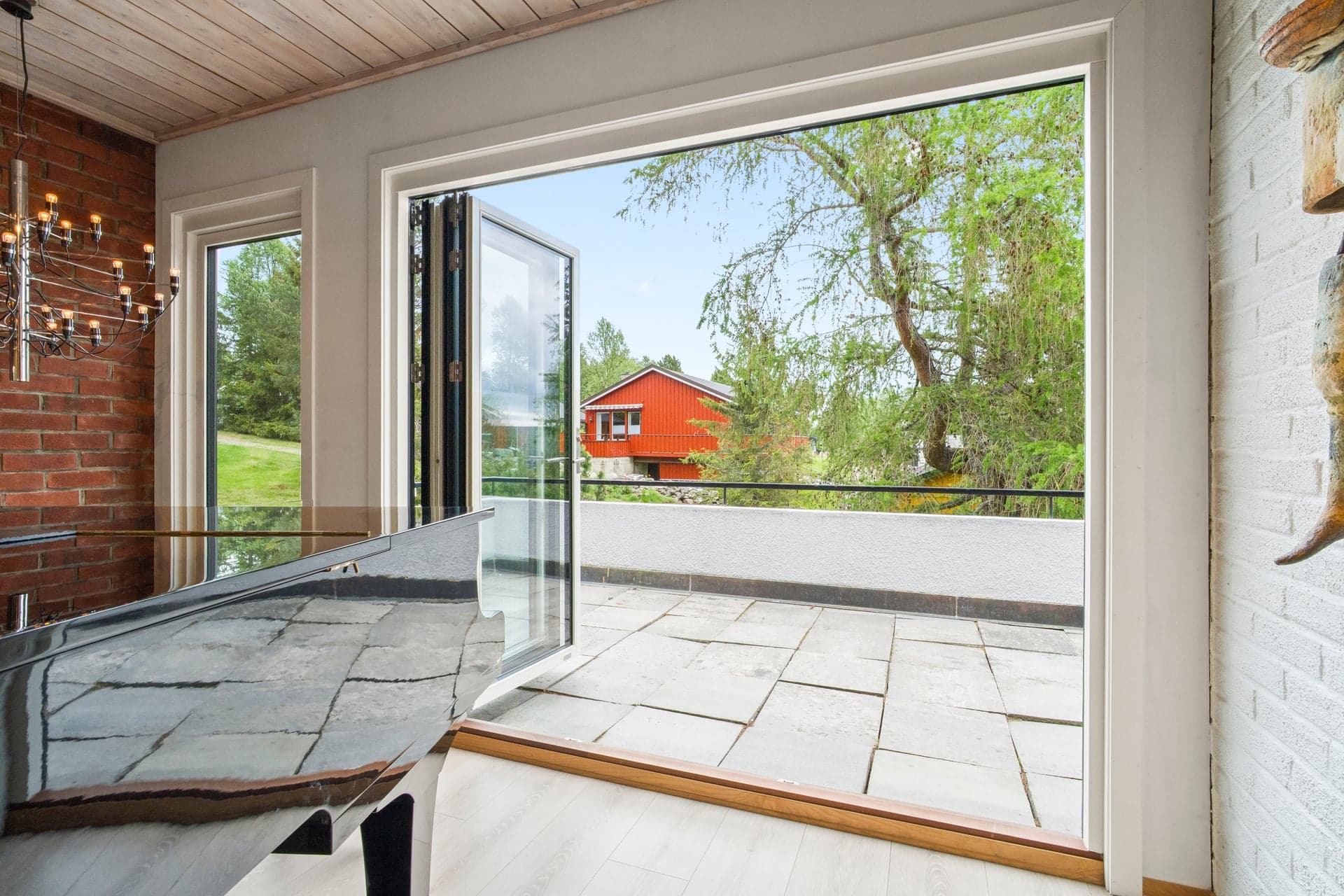 Fra allrommet er det utgang til en terrasse som strekker seg rundt flere sider av boligen.