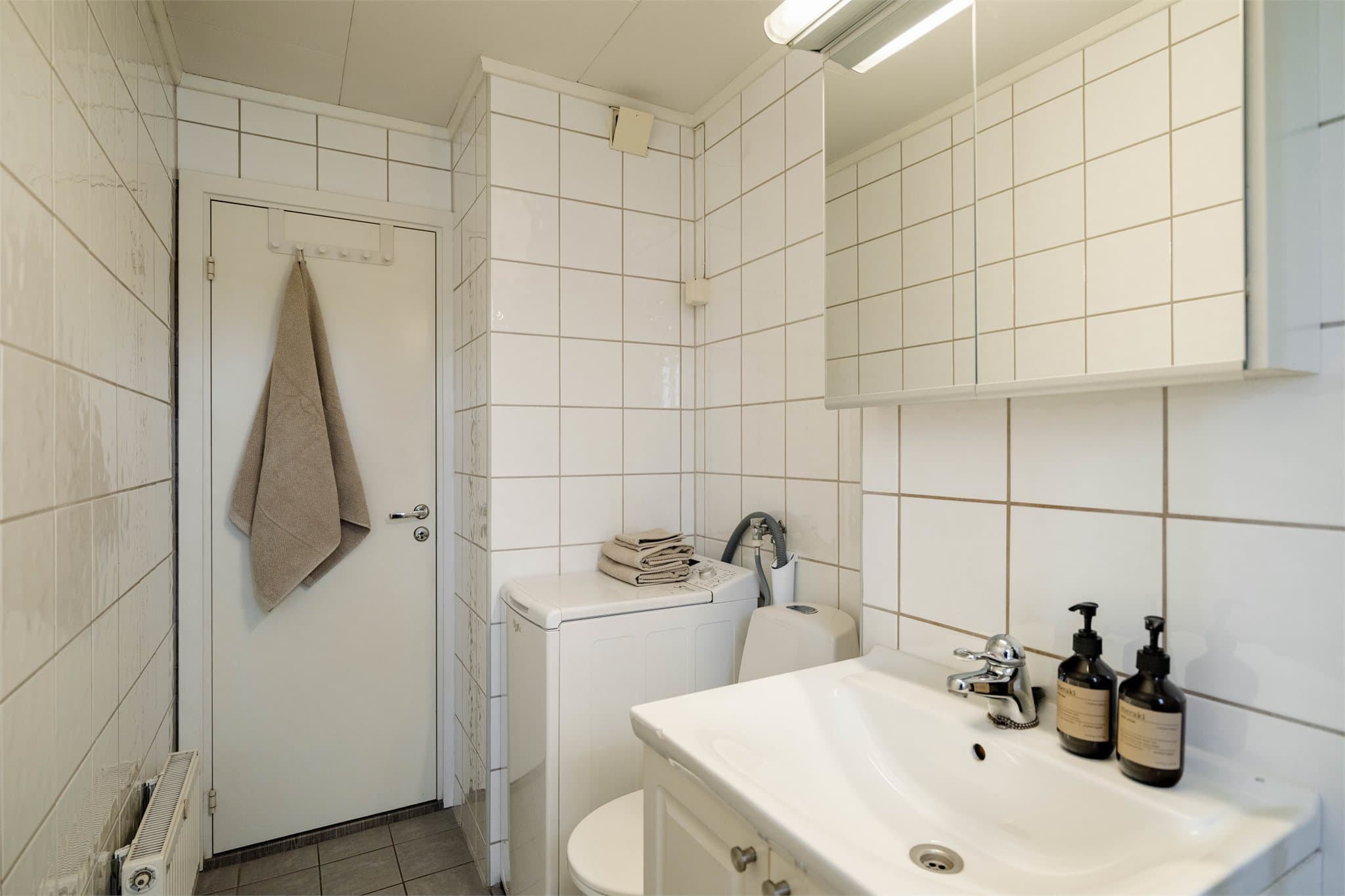 Flislagt bad/vaskerom med gulvvarme, dusjkabinett og opplegg for vaskemaskin.