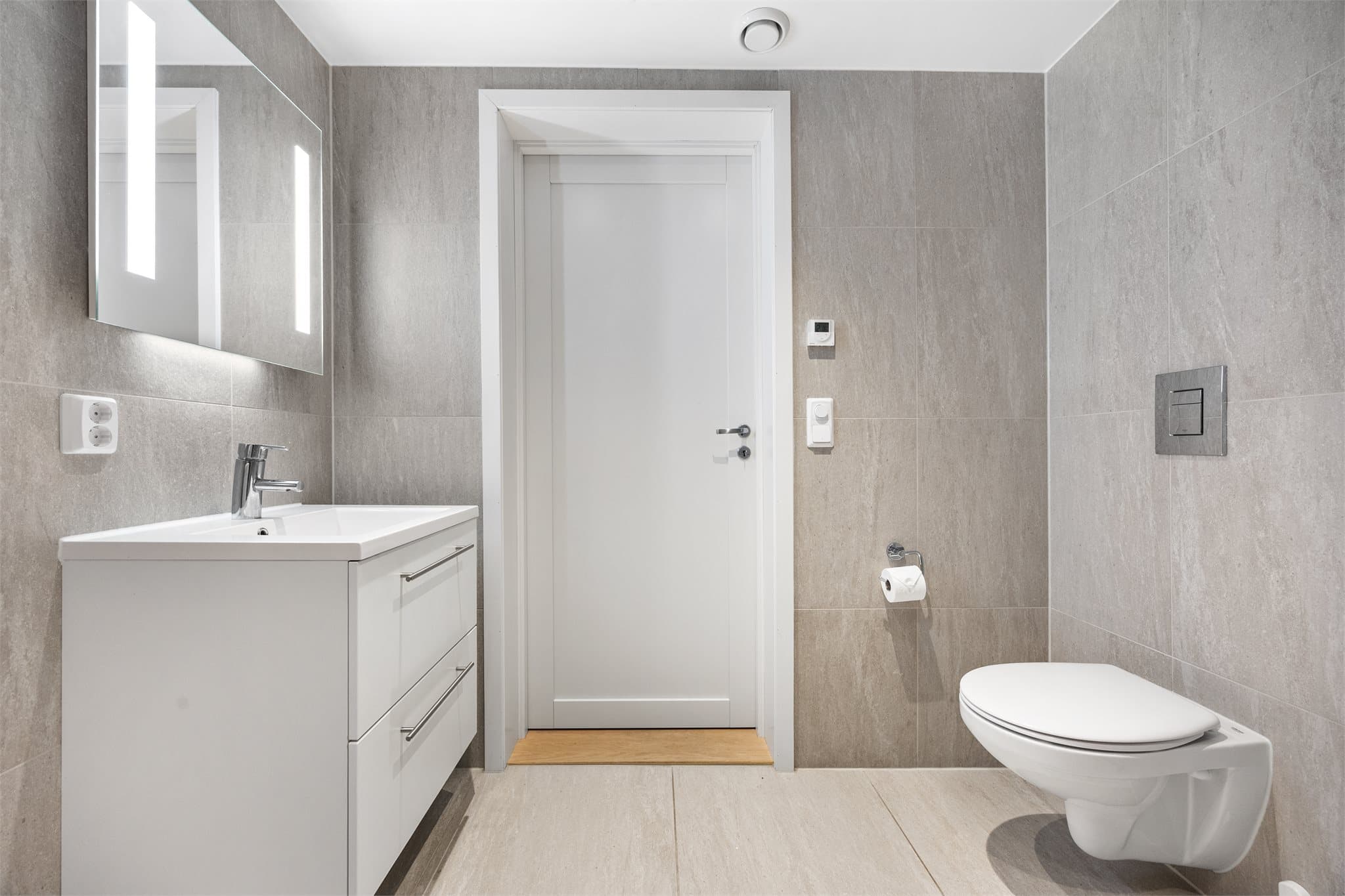 Innredning bestående av servant med underskap, speil med belysning, vegghengt toalett og dusjsone.