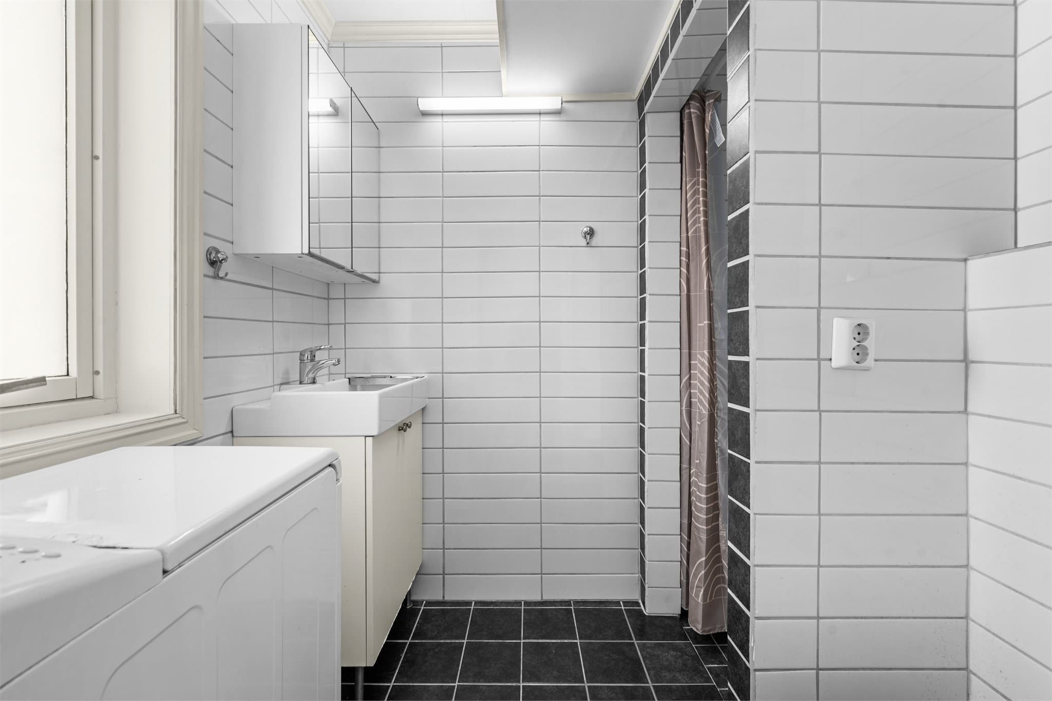 Baderom i hybeldel innredet med dusj, servant på skapseksjon med overspeil, toalett og opplegg for vaskemaskin. Tidligere vaskerom/bod, rommet er ikke bruksendret. Søknad er under behandling i kommunen, se salgsoppgave.