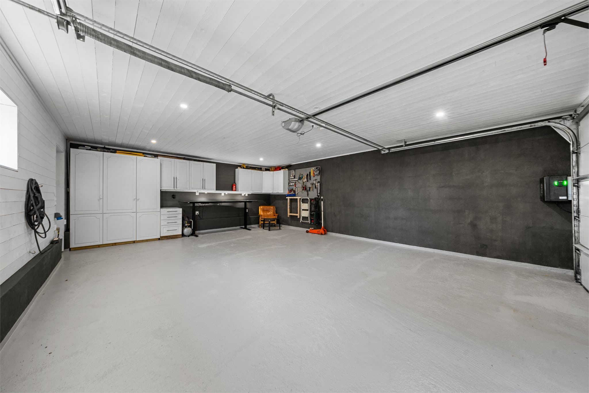 Dobbelgarasje med to elbilladere (en ekstra lader er montert ute). Garasjen har spotter i tak og rikelig med arbeidsplass - perfekt for deg med bilhobby eller behov for snekkerverksted.