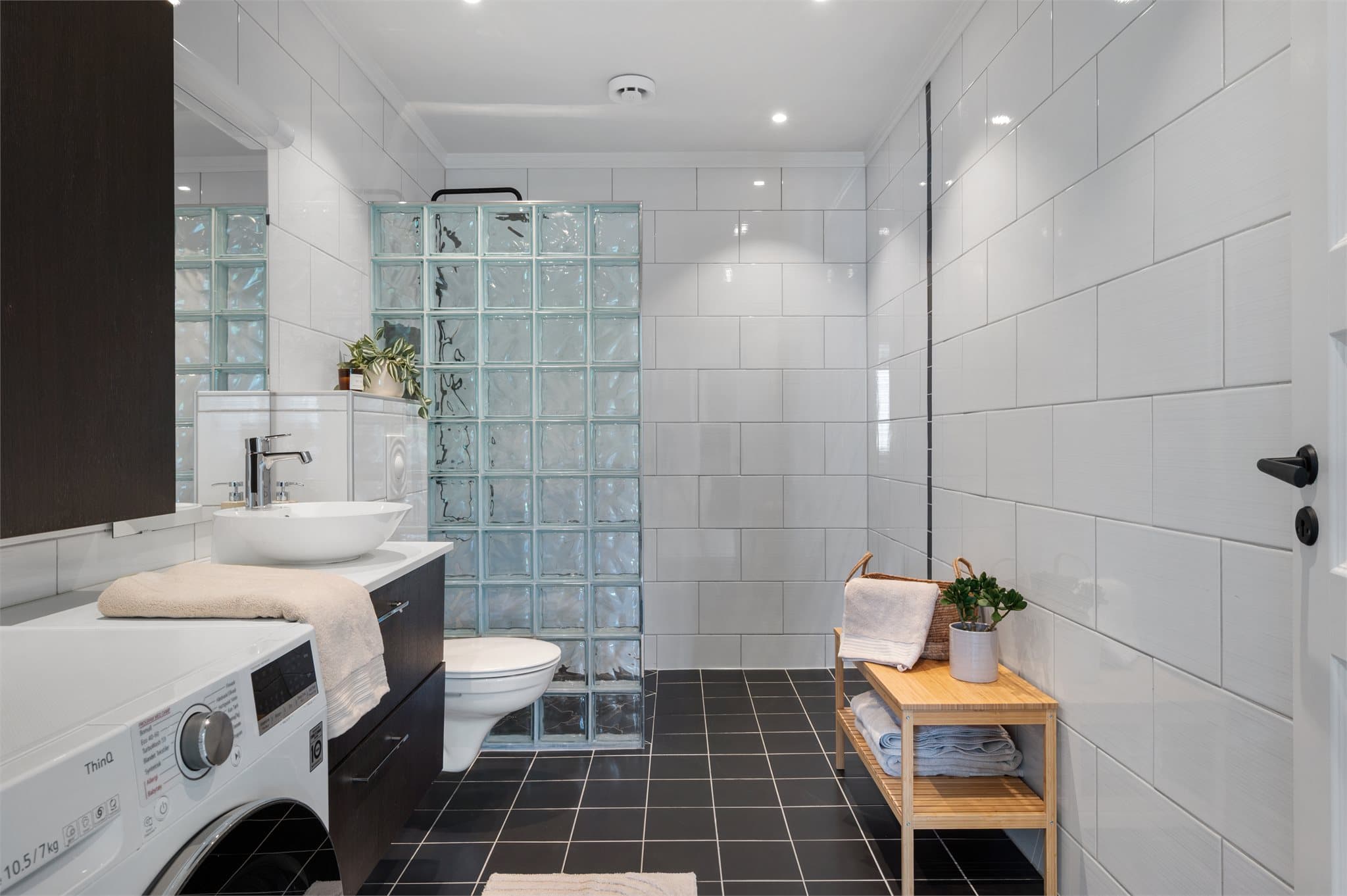 Badet måler 7m² og inneholder veggehengt toalett, benkeskap med servant, opplegg for vaskemaskin og dusjhjørne