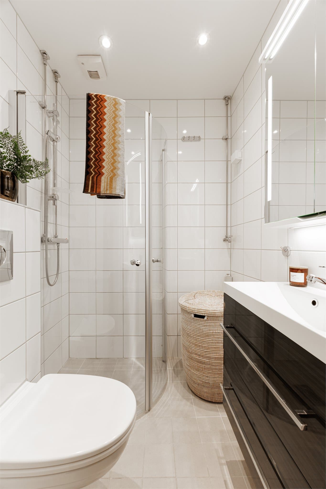 Badet fremstår lyst og tidløst med lyse fliser og en praktisk planløsning. Baderomsinnredningen består av benkeskap med glatte fronter samt veggskap med speilfronter som gir god oppbevaringsplass.