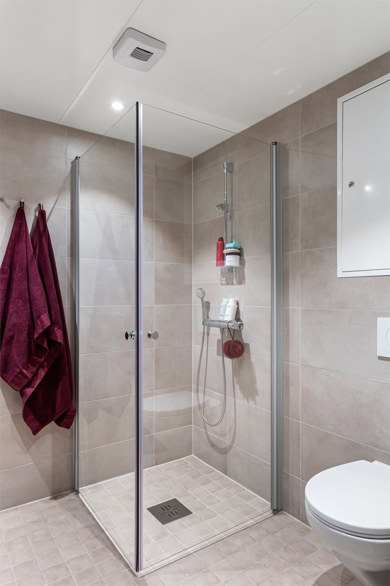 Badet er utstyrt med vegghengt toalett, dusjhjørne med glassdører og downlights i taket.