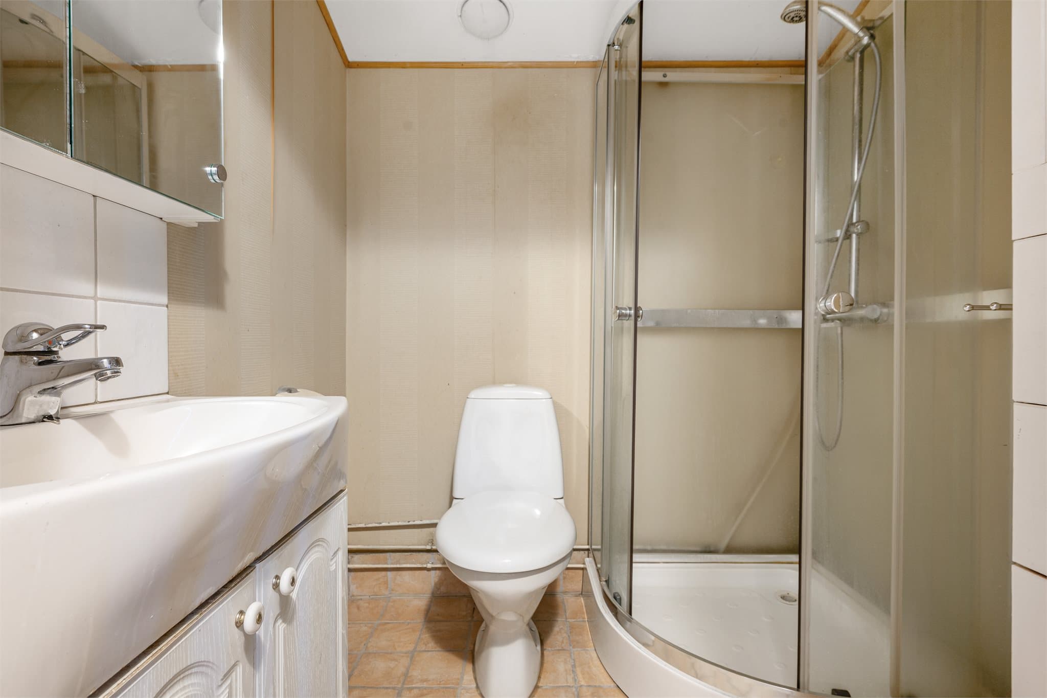 Badet i 1.etasje har fliser på gulv over gulvvarme. Innredet med helservant på skapseksjon, speilskap, klosett og dusjkabinett.