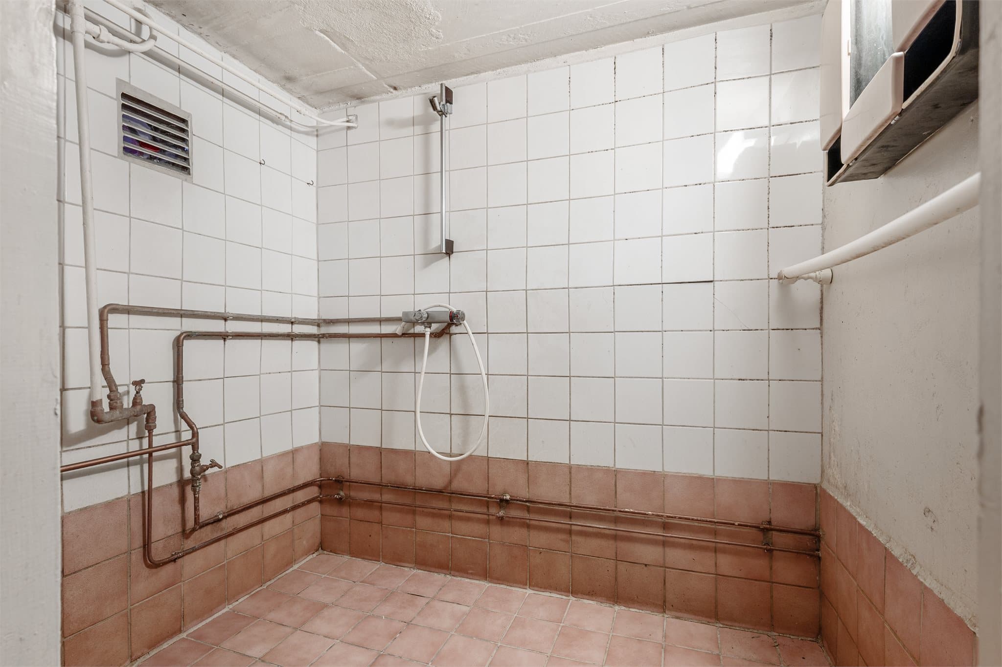 Flislagt sanitærrom med dusj på vegg.