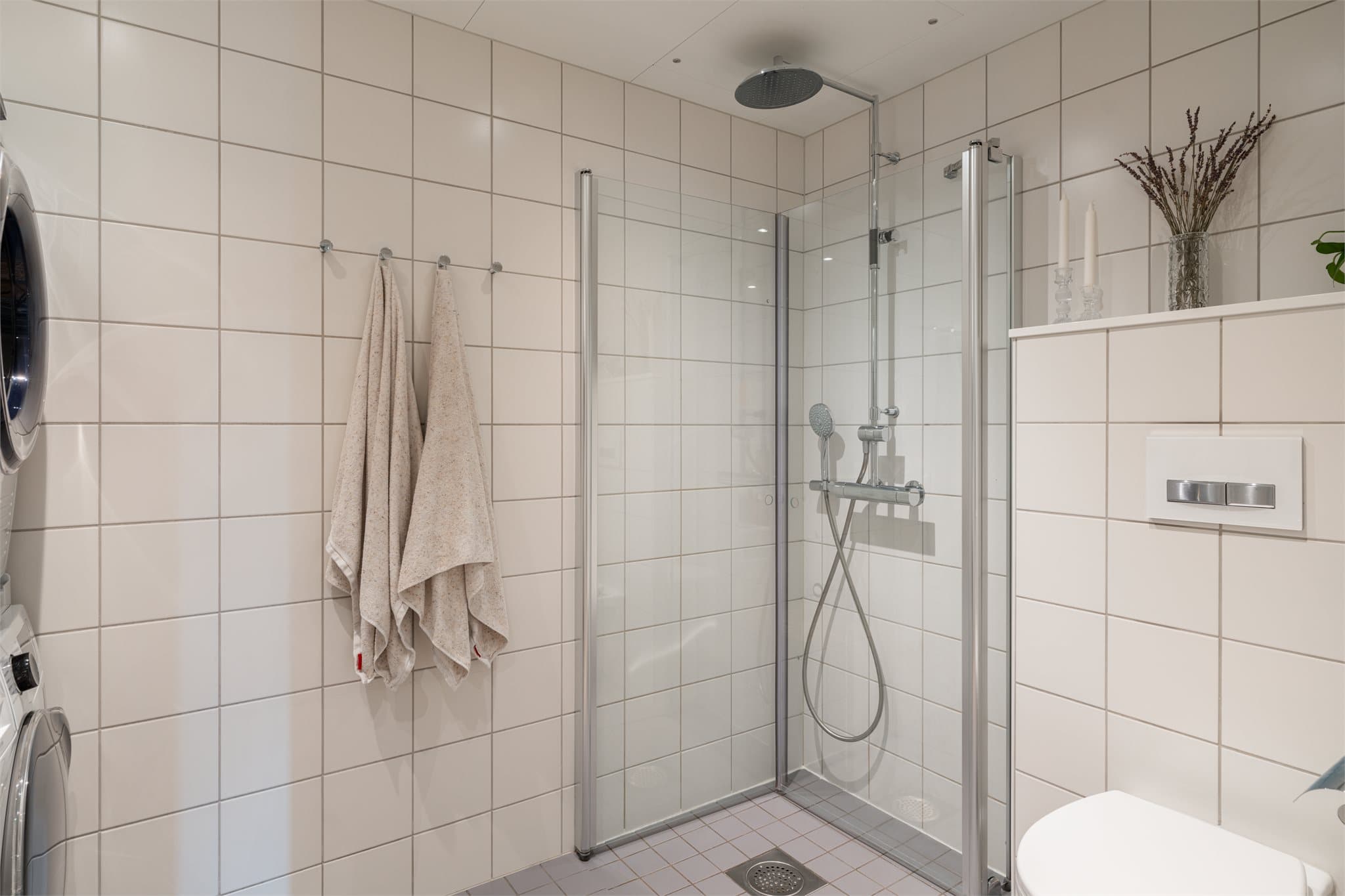 Badet er innredet med dusj på gulv med dusjdører i herdet glass.