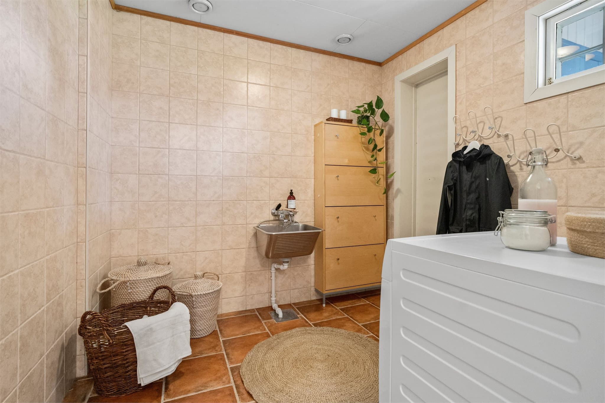 Praktisk, flislagt vaskerom med utslagsvask og opplegg for vaskemaskin.