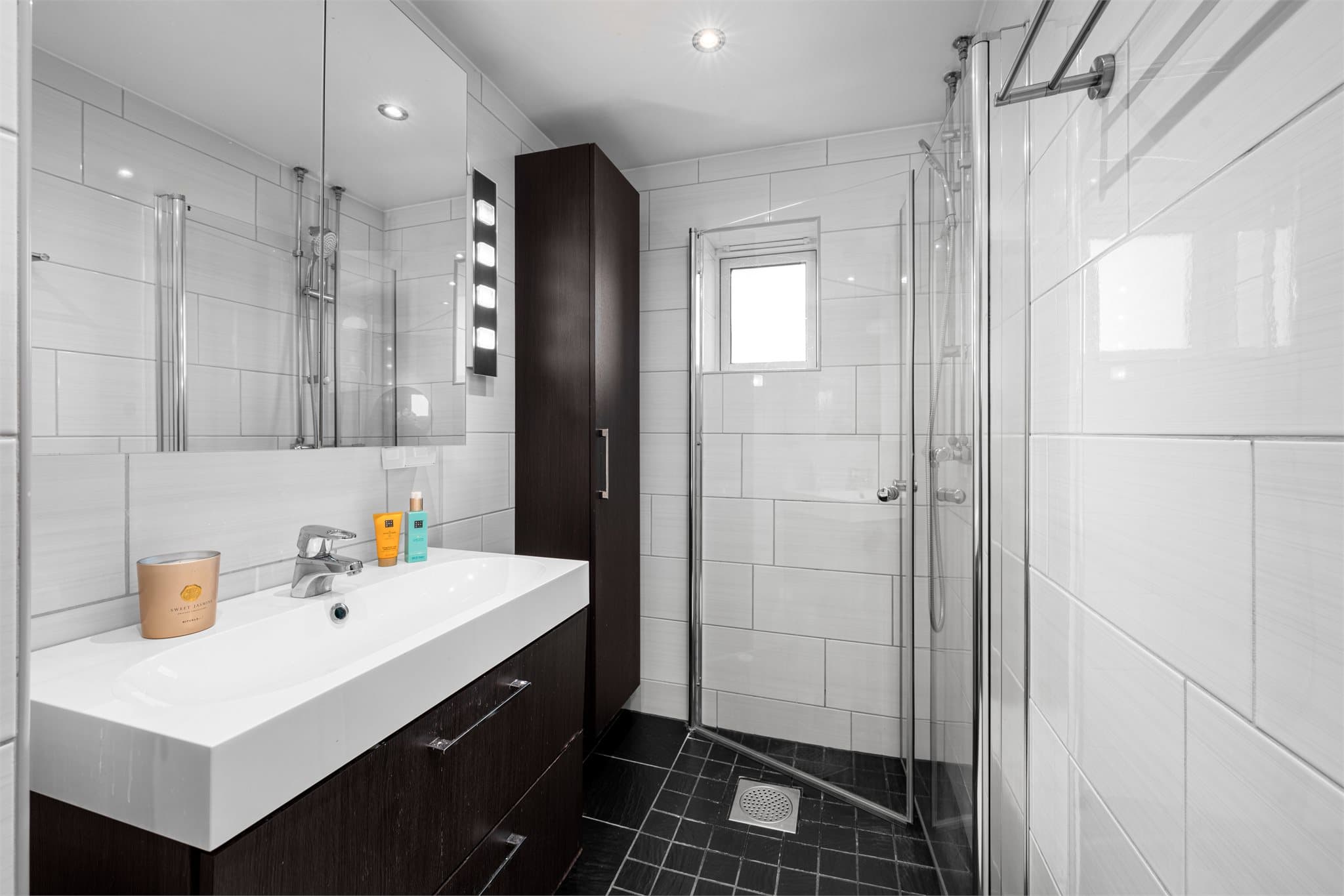 Badet er utstyrt med dusjhjørne, toalett og servant med over og underskap.