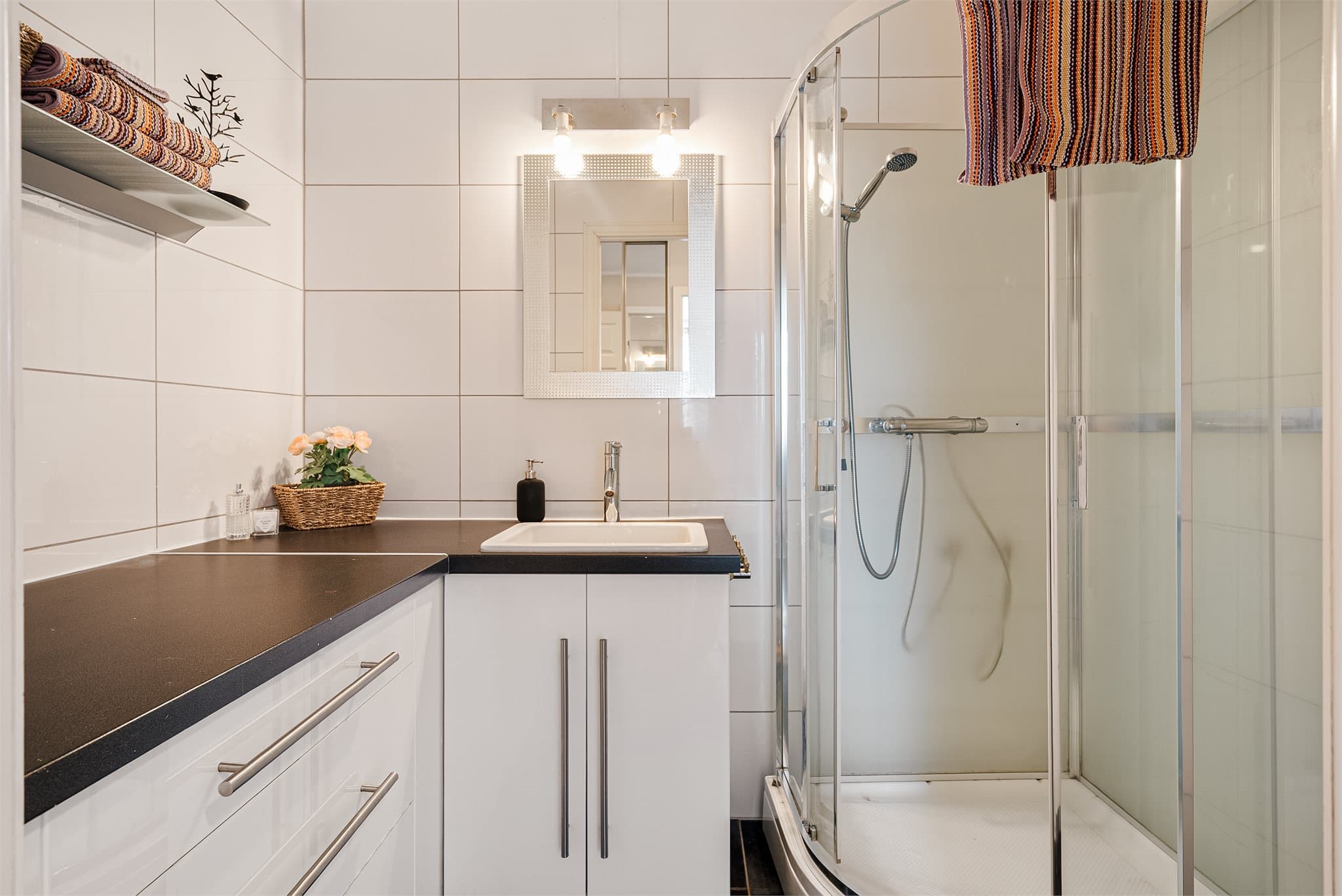 Lyst og innbydende bad med store fliser, god oppbevaringsplass, dusjkabinett og varmekabler i gulv.