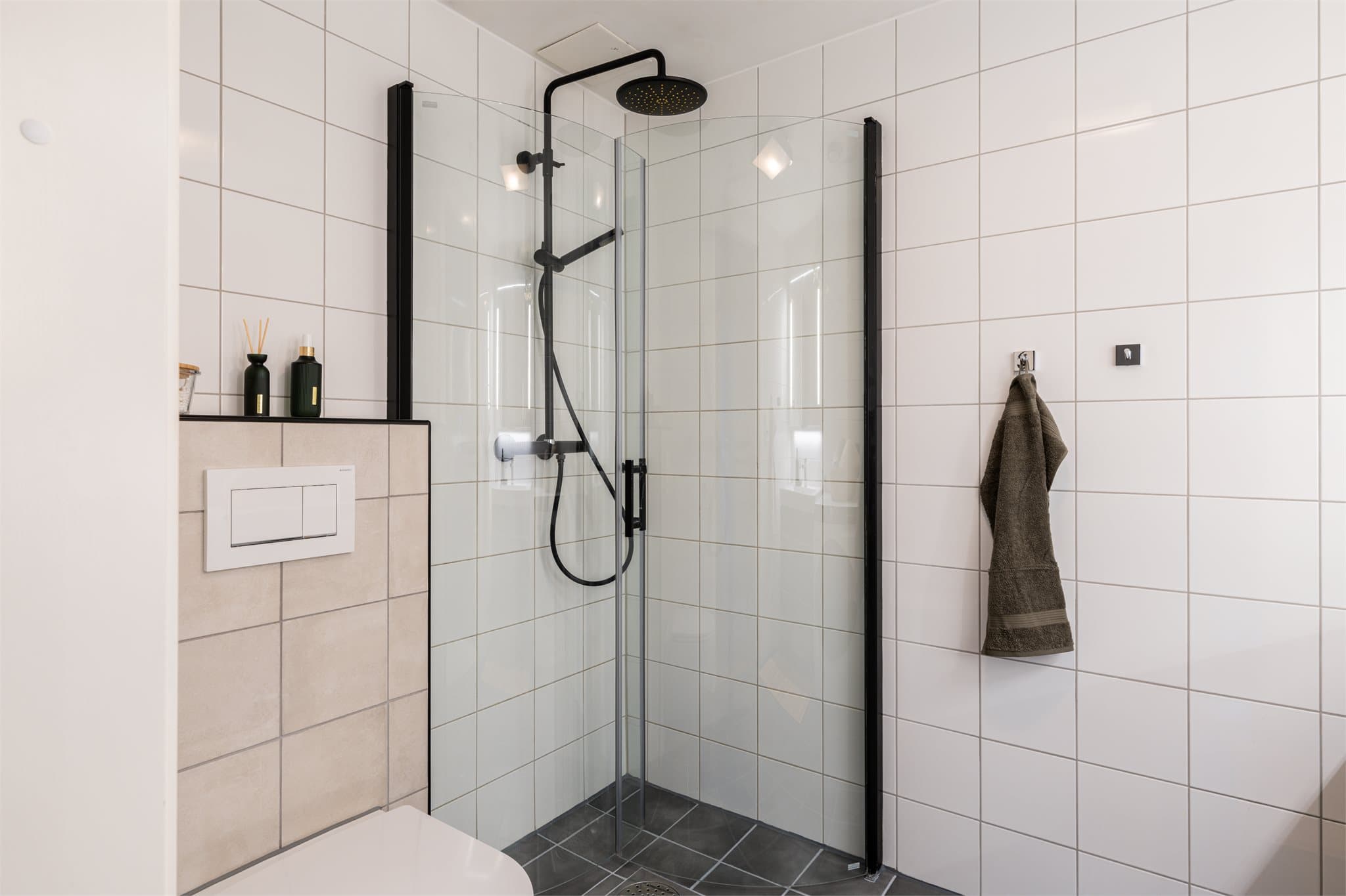 Romslig dusjnisje bak innfellbare dusjdører i herdet glass.