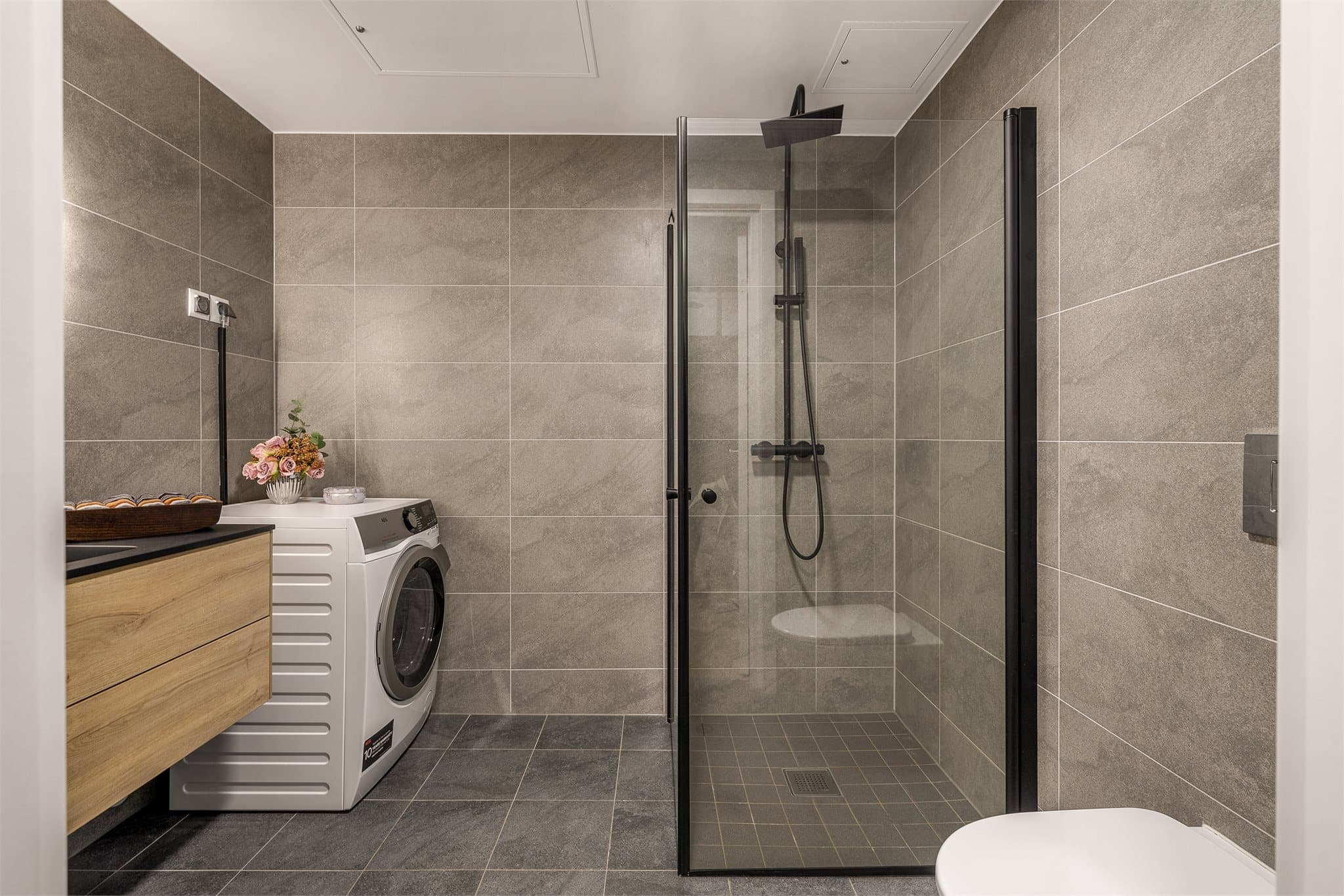 Lekkert baderom med vegghengt toalett, servant på skuffeseksjon og dusjløsning med regnfall.