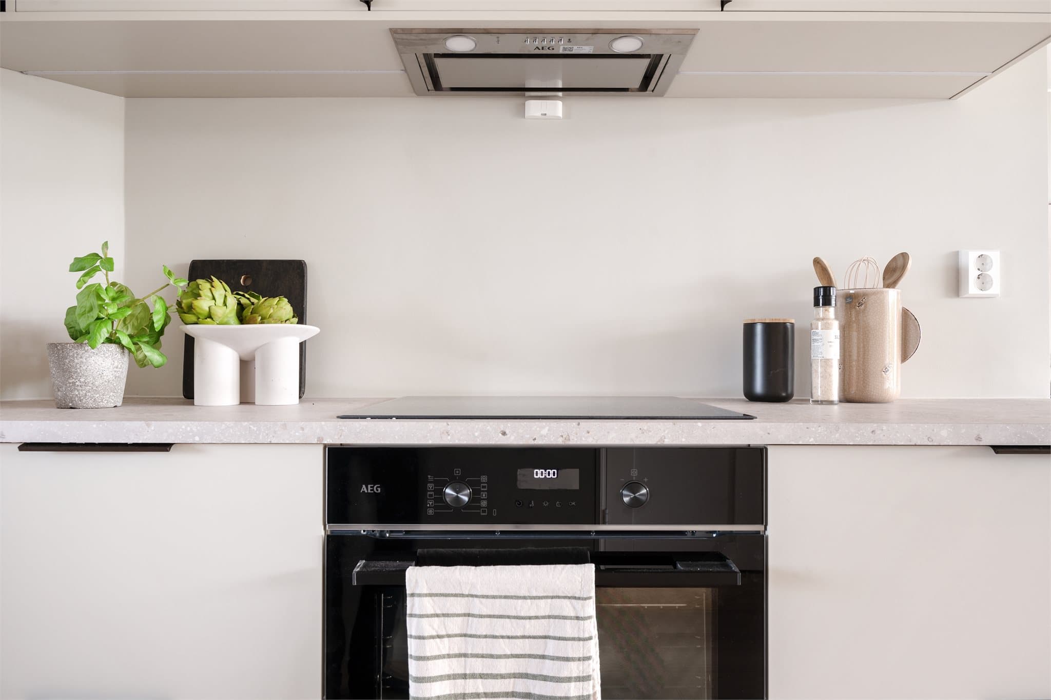 AEG ventilator med kullfilter kommuniserer med induksjonstoppen under bruk – en moderne detalj som understreker den høye utstyrstandarden. Det er montert komfyrvakt under overskap.