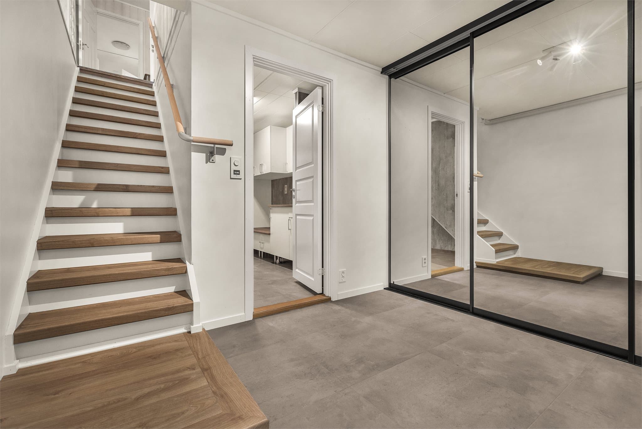 Stor skyvedørsgarderobe med speilfronter og innvendig trapp til hovedplanet.