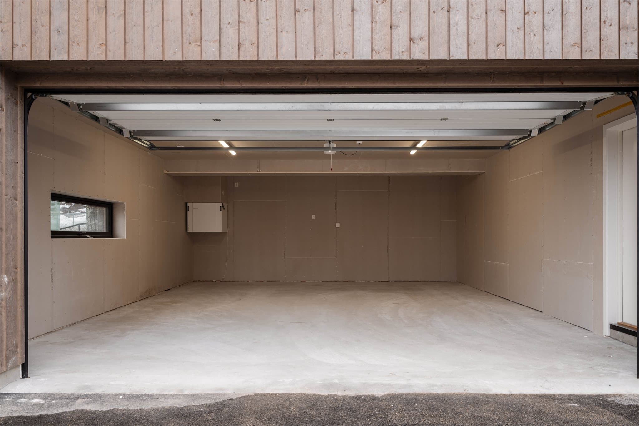 Garasjen leveres med OSB-plater på vegger og tak, samt garasjeport i dempet sort (NCS 8500). Herfra er det dør rett inn til boligen.