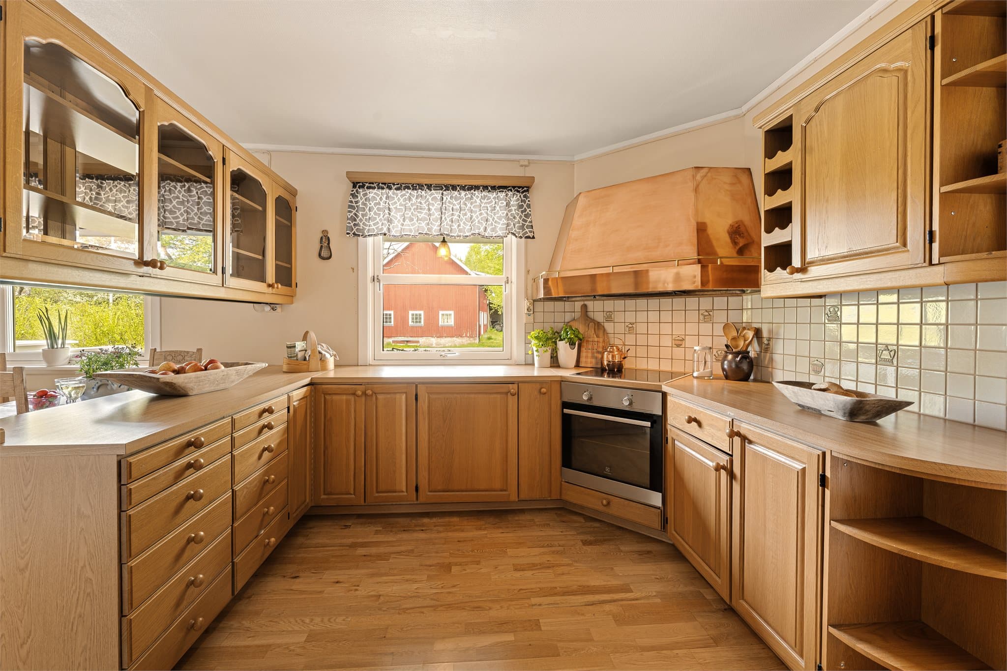 Den tradisjonelle kobberventilatoren gir kjøkkenet en sjarmerende og rustikk stil som harmonerer fint med de varme treflatene og den klassiske innredningen.