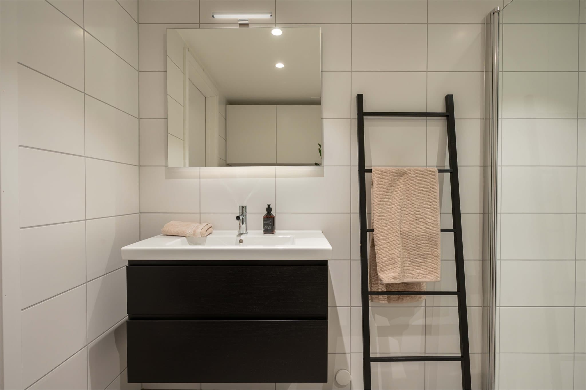 Badet er utstyrt med en moderne servantinnredning med skuffer og et speil med integrert belysning.