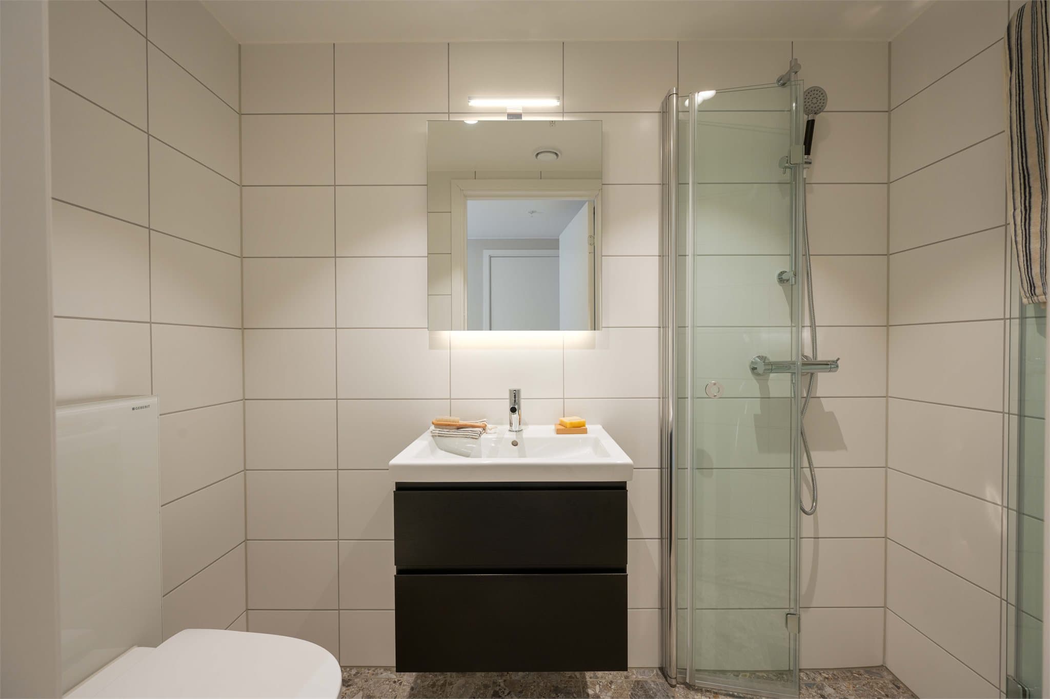 Bad 2 er flislagt og innredet med servant, toalett og dusjhjørne med innfellbare glassdører.