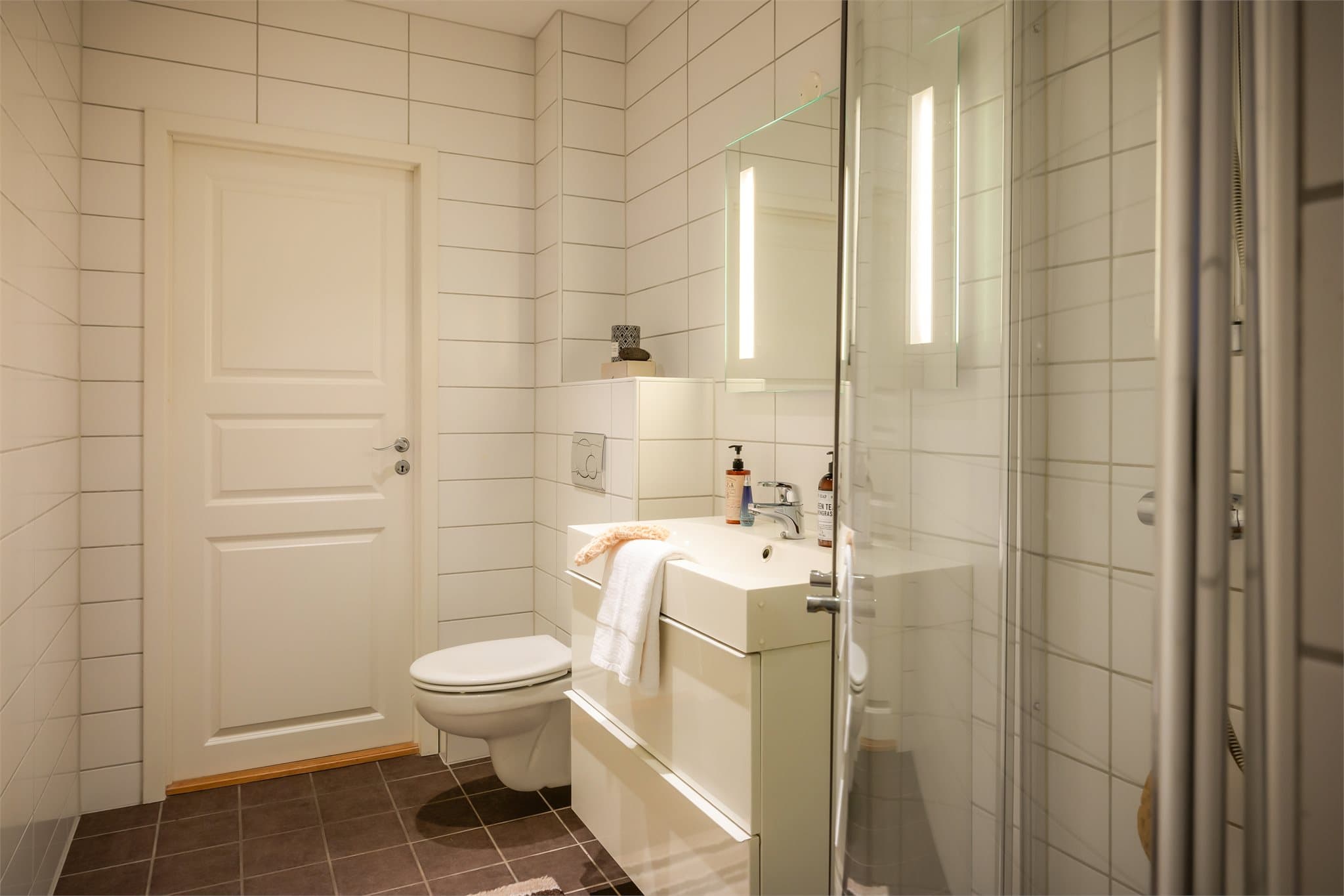 - Badet er innredet med vegghengt toalett, heldekkende servant, speil med belysning og innfellbare dusjdører -