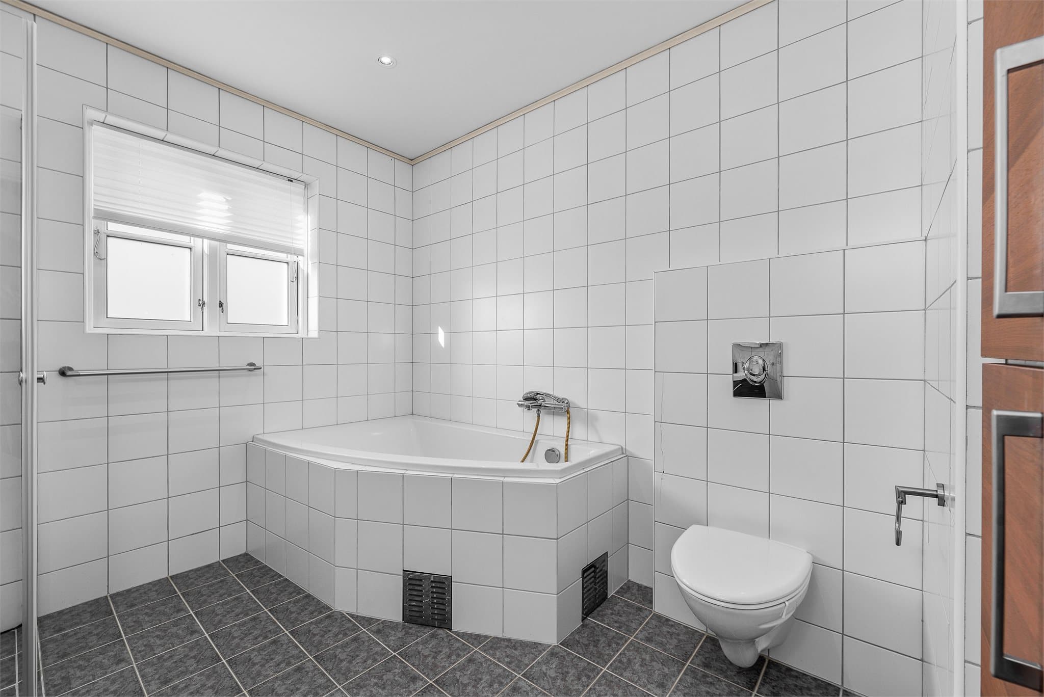 Badet er innredet med helservant på skuffeseksjon, vegghengt toalett, dusjhjørne og badekar.