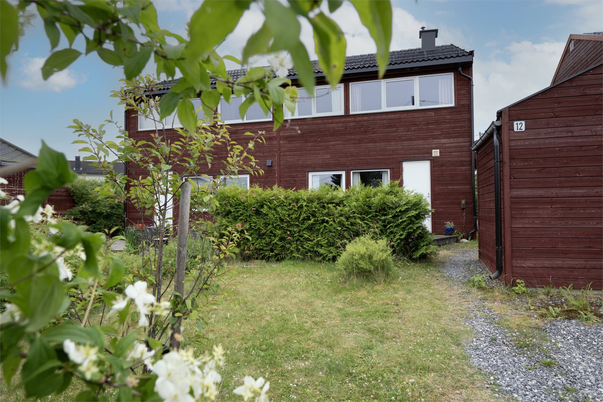 Den hyggelige inngangssiden byr på en lettstelt hage, praktisk utebod og egen kjøkkeninngang til vaskerom fra markterrassen på forsiden av boligen.