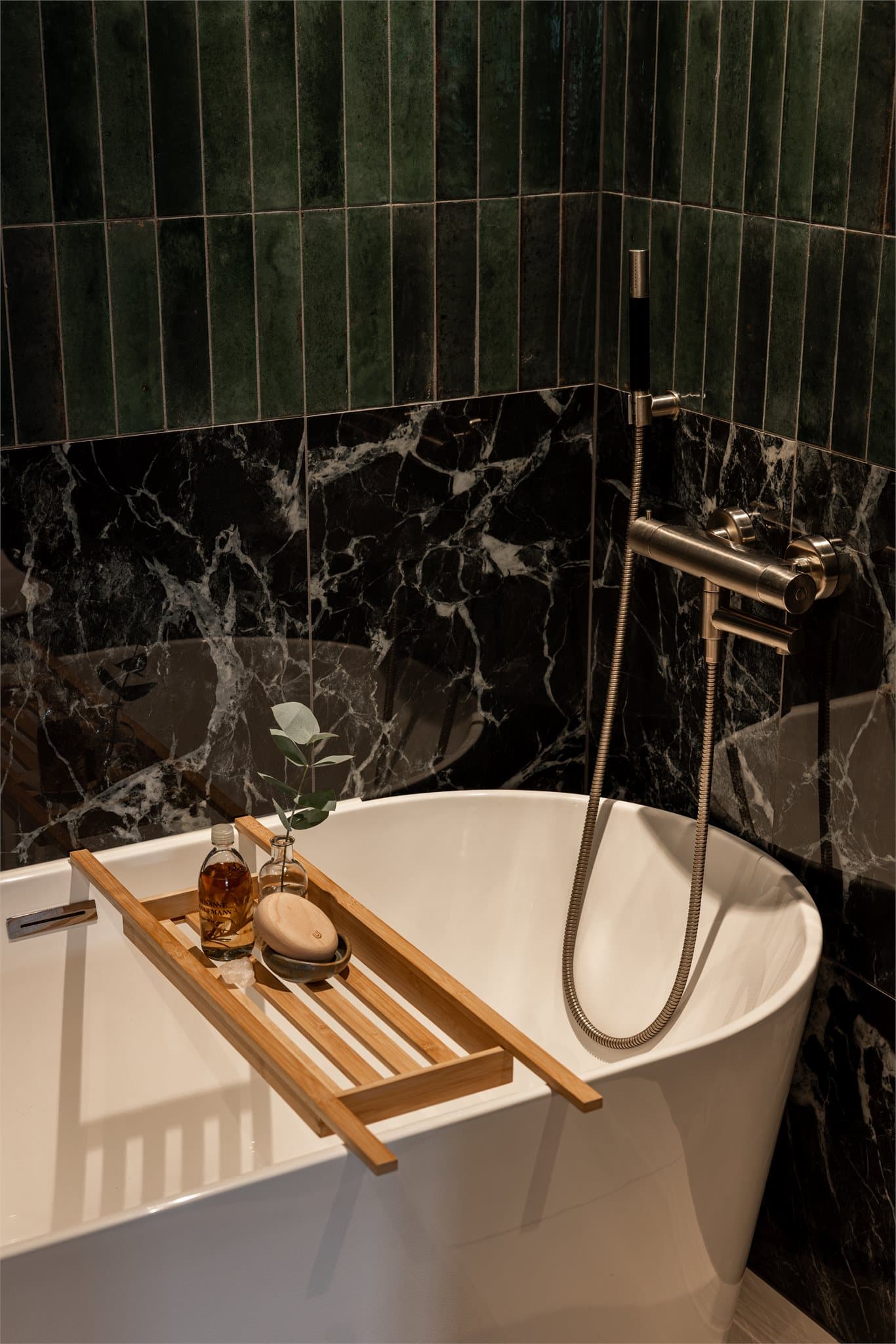 Badet i første etasje har en mørk, elegant fargepalett med grønne innslag og et innbydende badekar for avslapning.