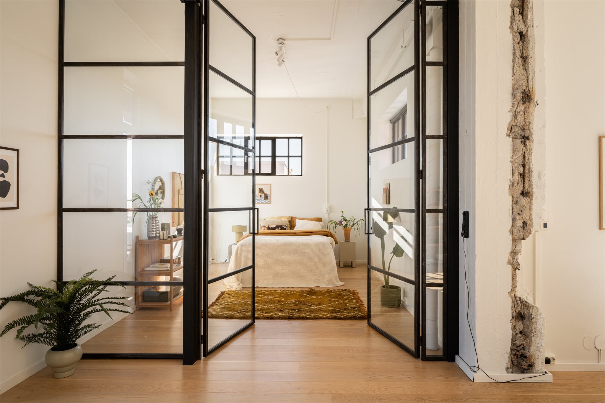 Del av stuen er delt av og innredet som et romslig soverom, avskjermet med påkostet elegant plassbygd glassvegg med doble glassdører. Legg merke til veggen på høyre side, et lite stykke historie i original mur fra den opprinnelige Vinfabrikken.