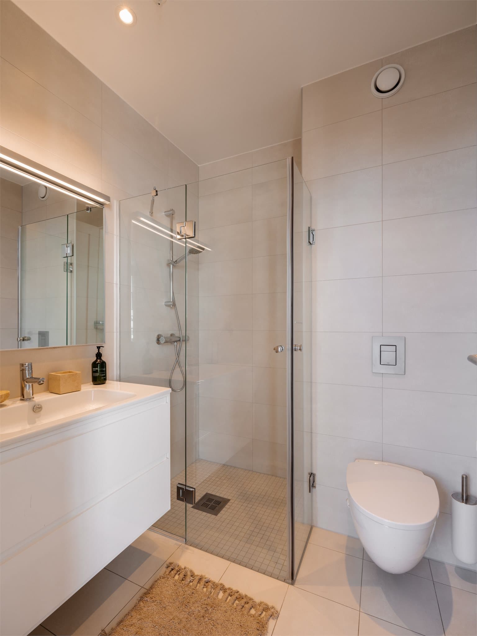 Leilighetens baderom i andre etasje er moderne og innbydende, med fokus på funksjonalitet og stil. Rommet er helfliset med elegante, lyse fliser på både gulv og vegger, noe som gir et rent og harmonisk uttrykk.