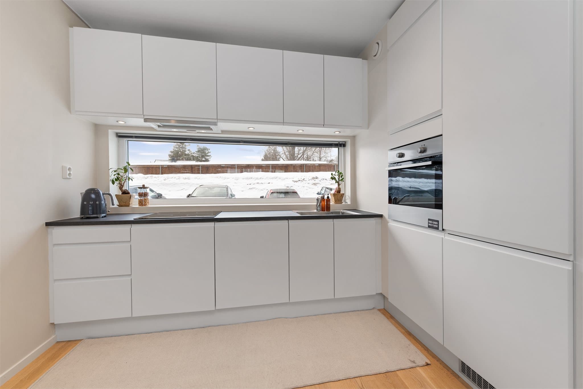 Lyst og moderne kjøkken med integrerte hvitevarer som kjøle-/fryseskap, oppvaskmaskin, stekeovn og platetopp