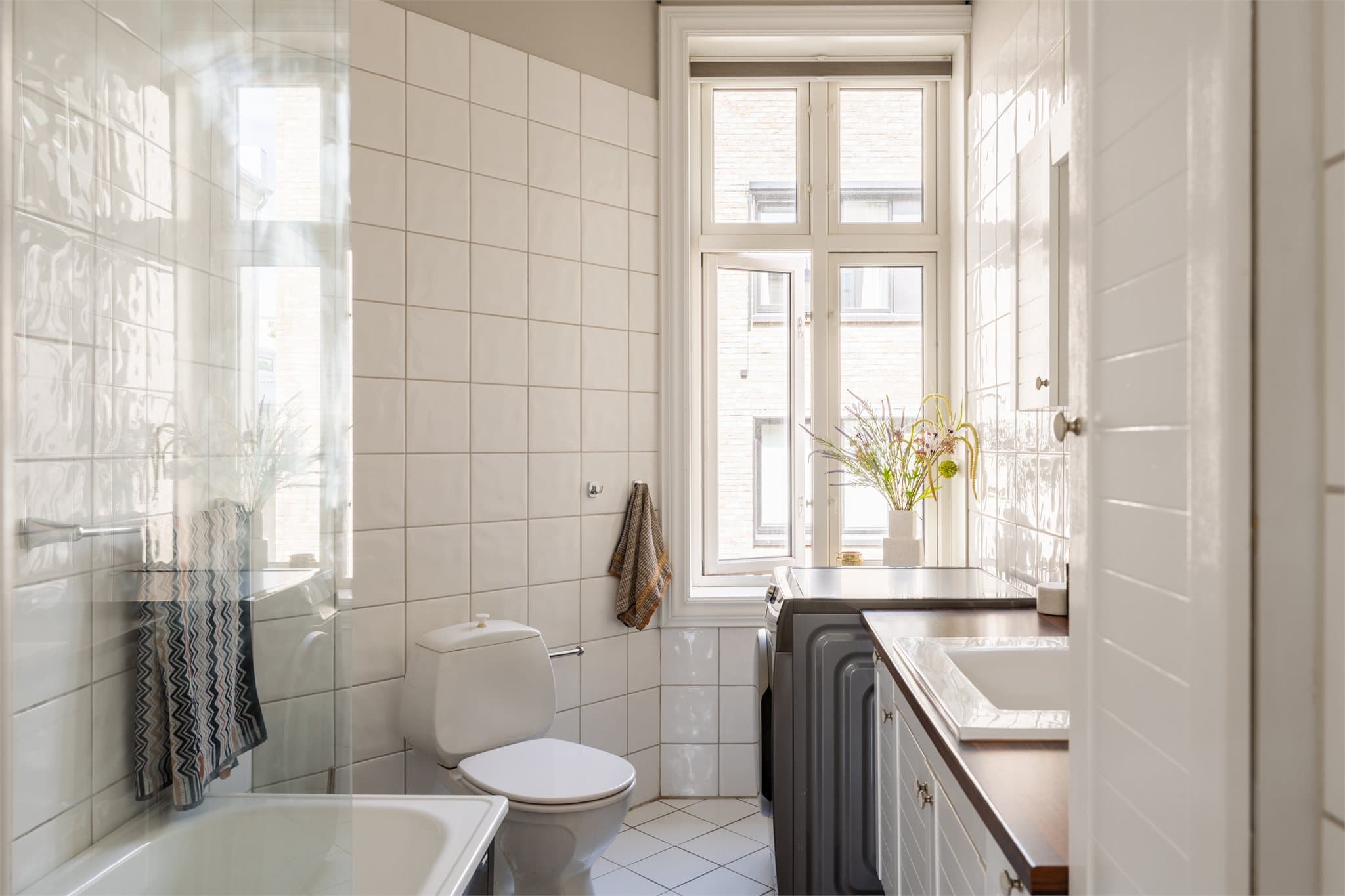 Badet har flislagte overflater, elektrisk gulvvarme og et stort vindu for naturlig dagslys.