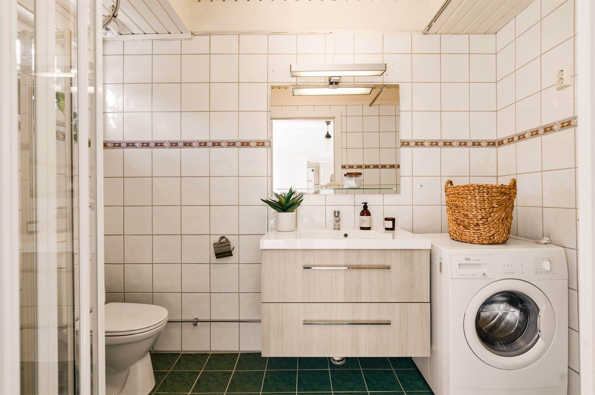 Badet er innredet med servantskap med glatte fronter, klosett, dusj på gulv og opplegg for vaskemaskin.