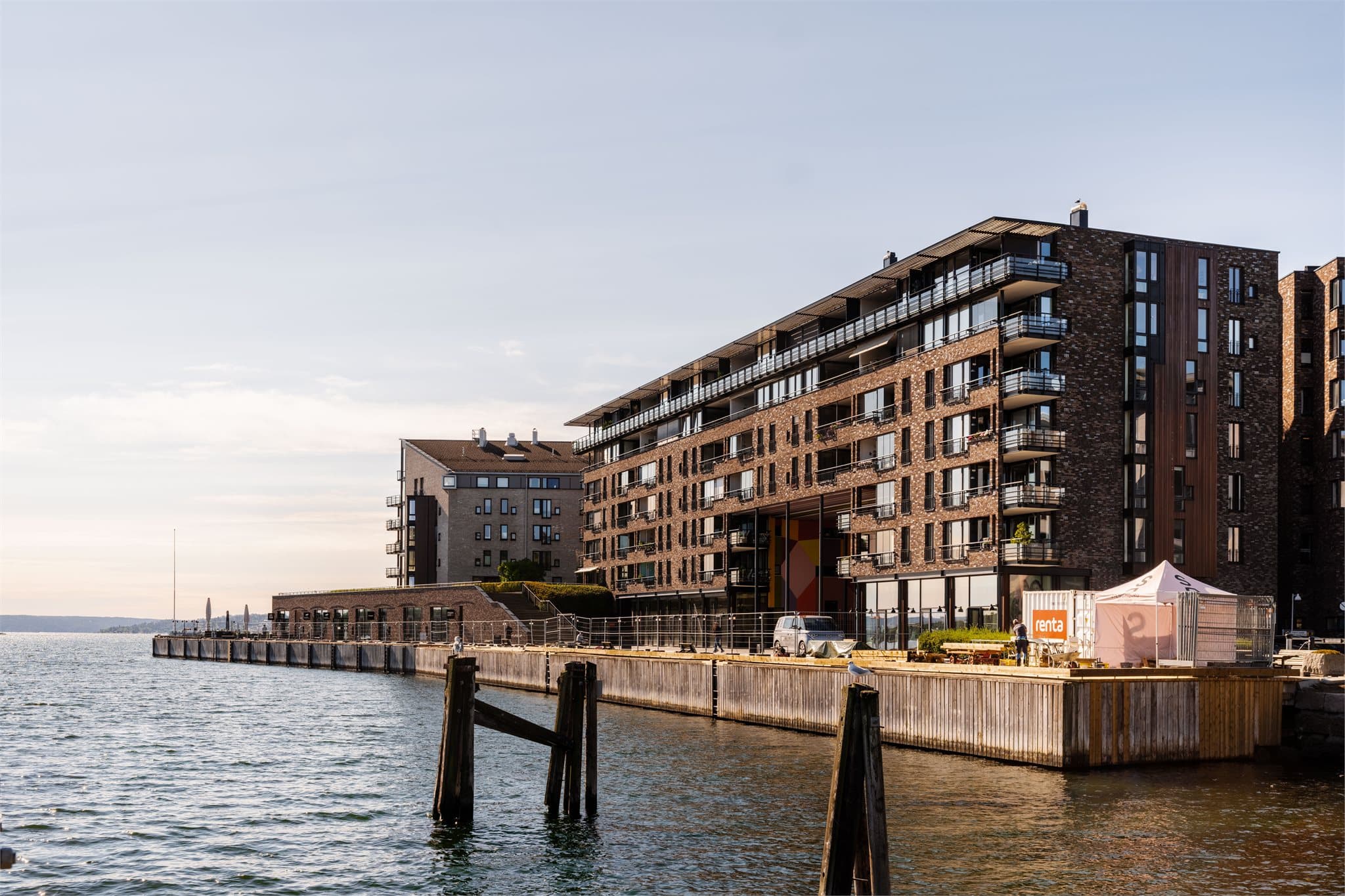 Bebyggelsen ligger helt ute ved sjøkanten med teglsteinsfasader og trebrygge langs vannet.