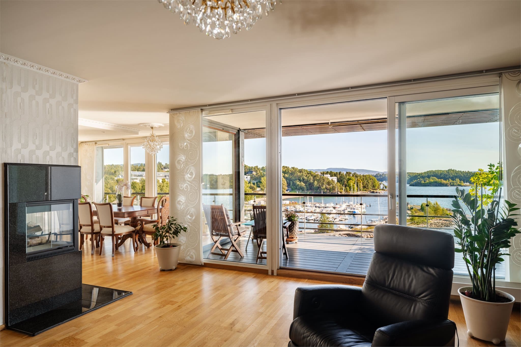Lys og åpen stue med store vindusflater mot fjorden og peisovn plassert sentralt i rommet.