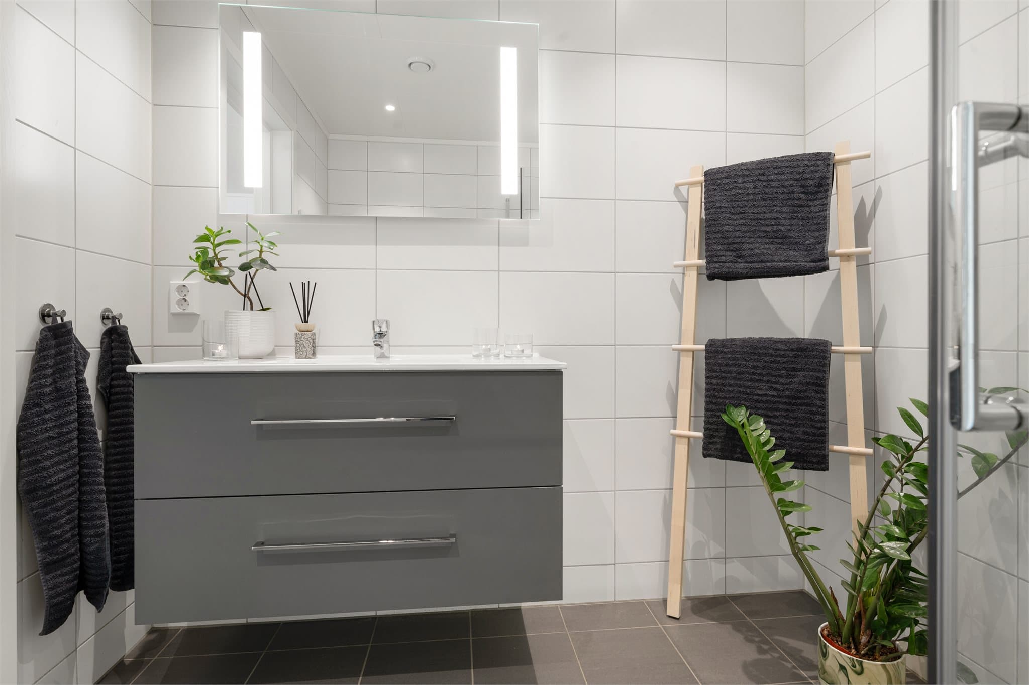 Badet er innredet med helservant på skuffeseksjon, dusjhjørne og vegghengt toalett.