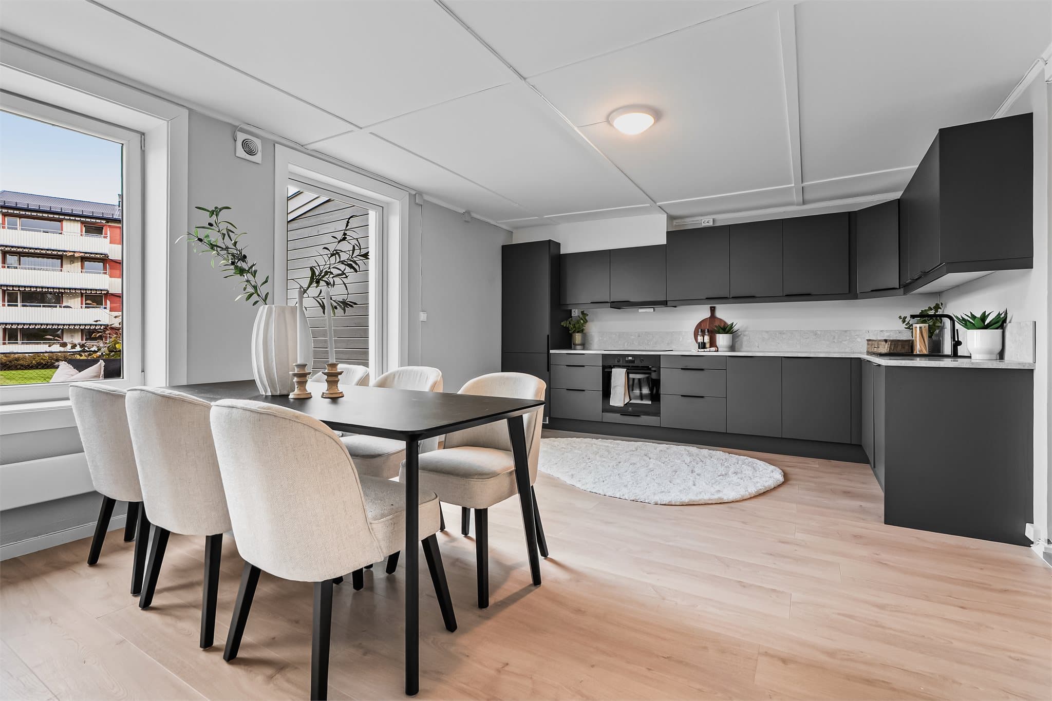 Gjennomgående plan med åpen kjøkkenløsning og spiseplass. Moderne mørke fronter, lys benkeplate og god tilgang til dagslys gjennom store vindusflater.