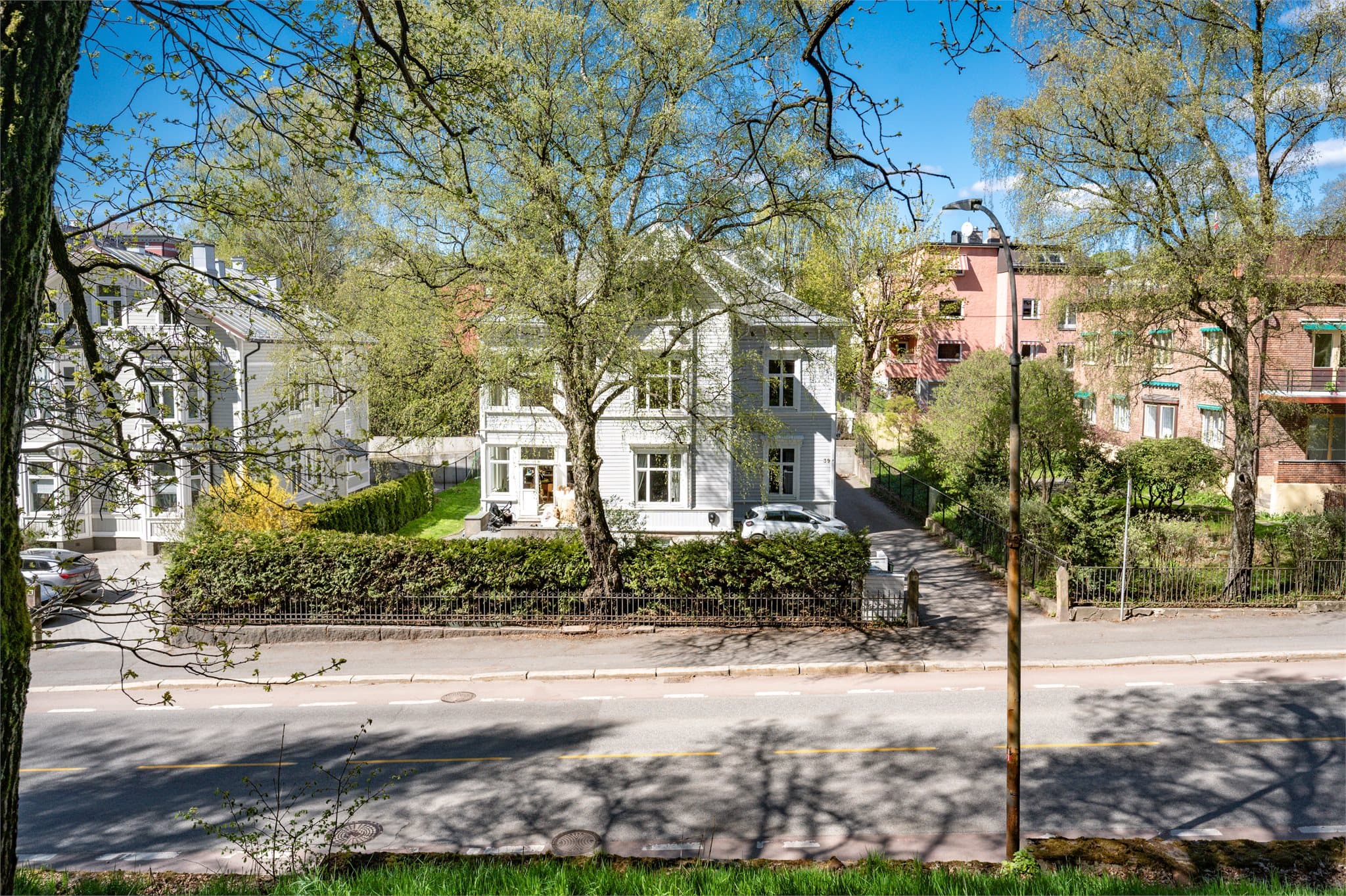 Villaen er idyllisk omkranset av felles hage med plen, hekker, trær og gjerde.