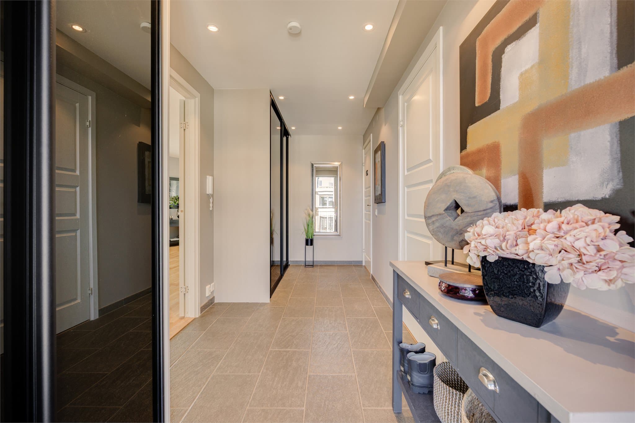 Romslig og innbydende entré med flislagt gulv og behagelig gulvvarme. Her møtes du av to praktiske skyvedørsgarderober med speilfronter som gir både god oppbevaringsplass og en følelse av ekstra rom.