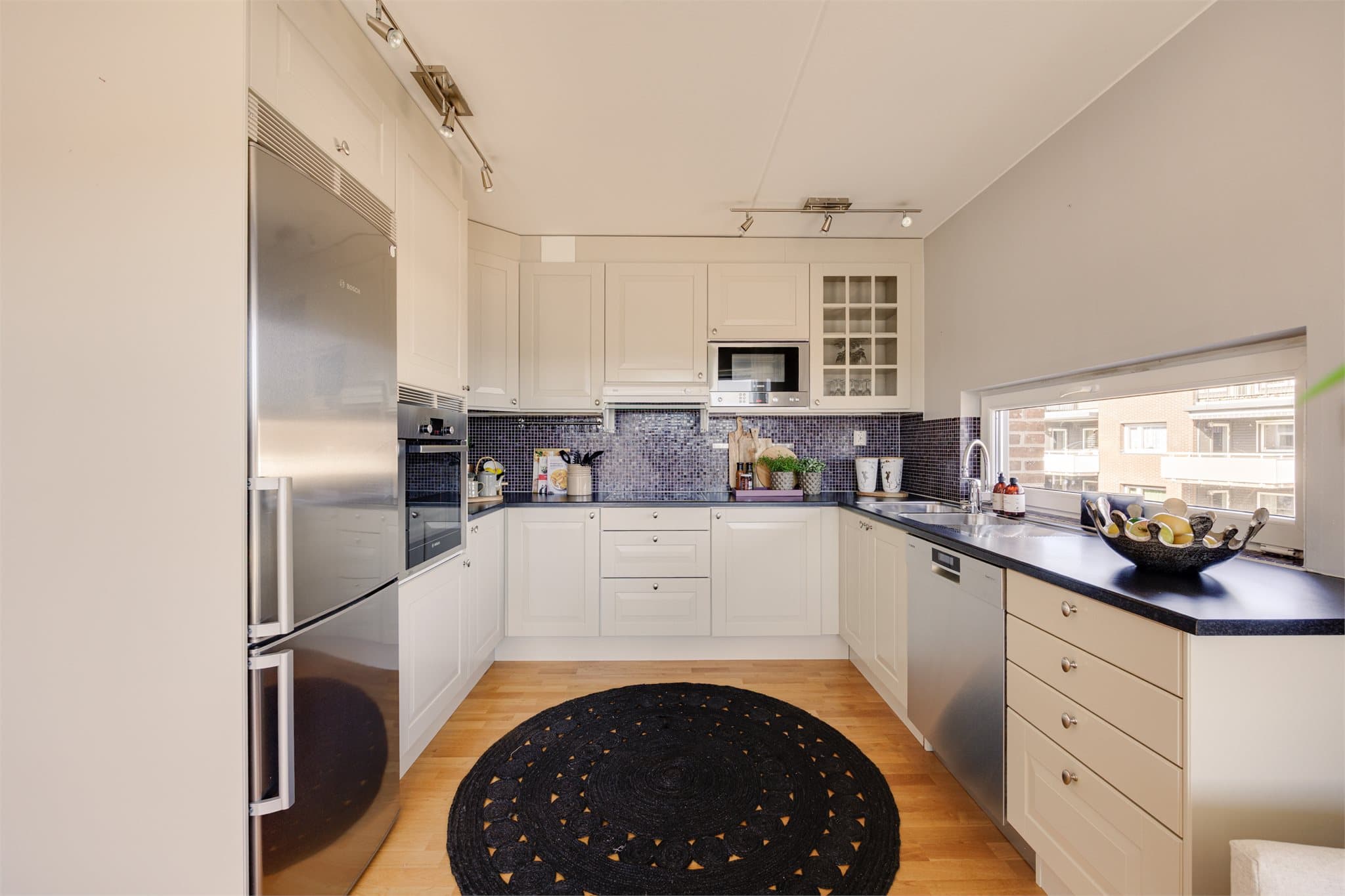 Det er fliser over benkeskap og laminat benkeplate med planlimt kum i rustfritt stål. Kjøkkenet er utstyrt med integrert induksjonstopp, stekeovn og mikrobølgeovn, samt ventilator med avtrekk til ventilasjonskanal. Det er også opplegg for oppvaskmaskin.