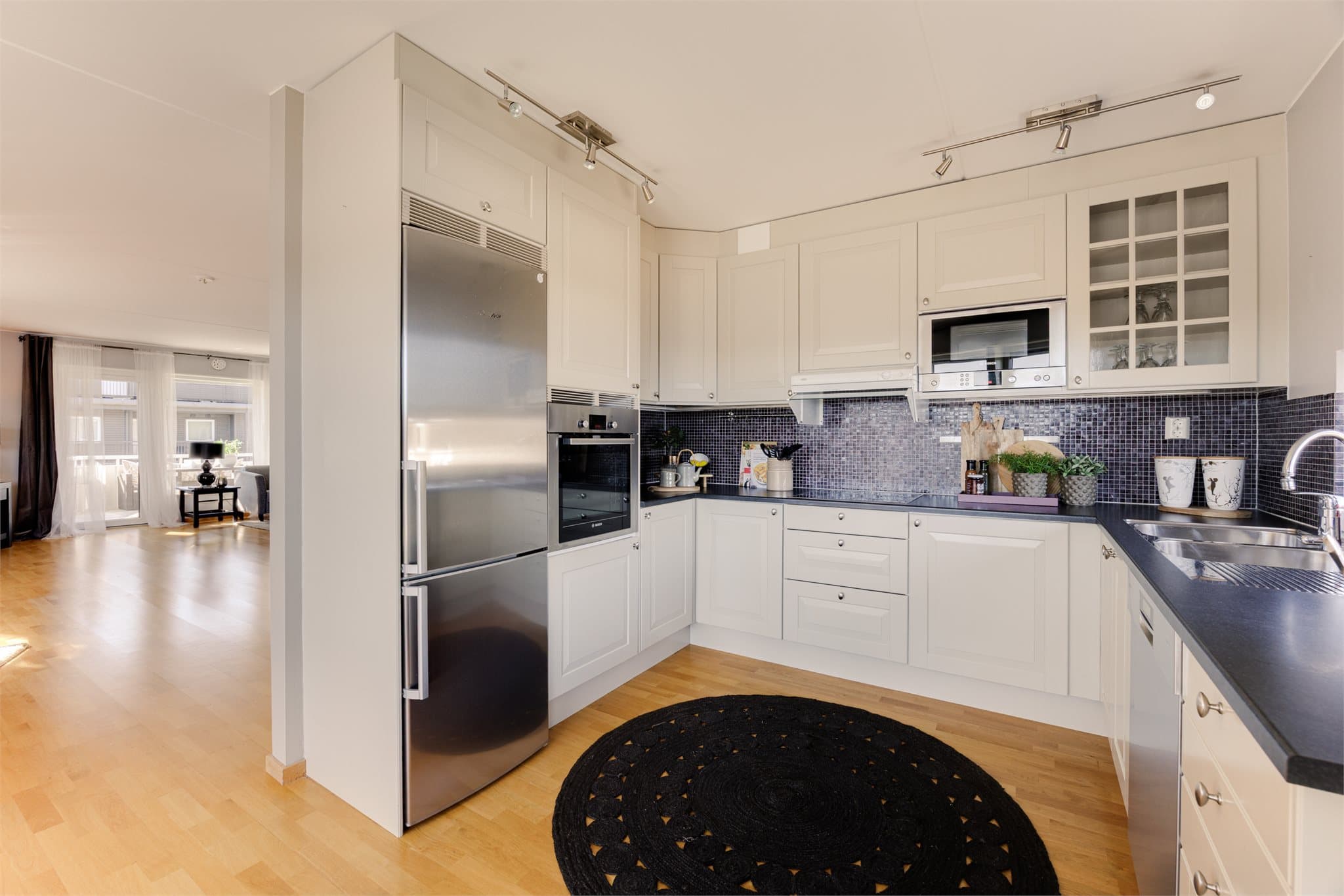 Klassisk, hvitt og tidløst kjøkken med delvis åpen løsning mot stuen. En skjermende vegg gir en praktisk inndeling, slik at kjøkkenet kan holdes mer privat ved behov.
Kjøkkeninnredningen har profilerte fronter og enkelte overskap med glassfronter.