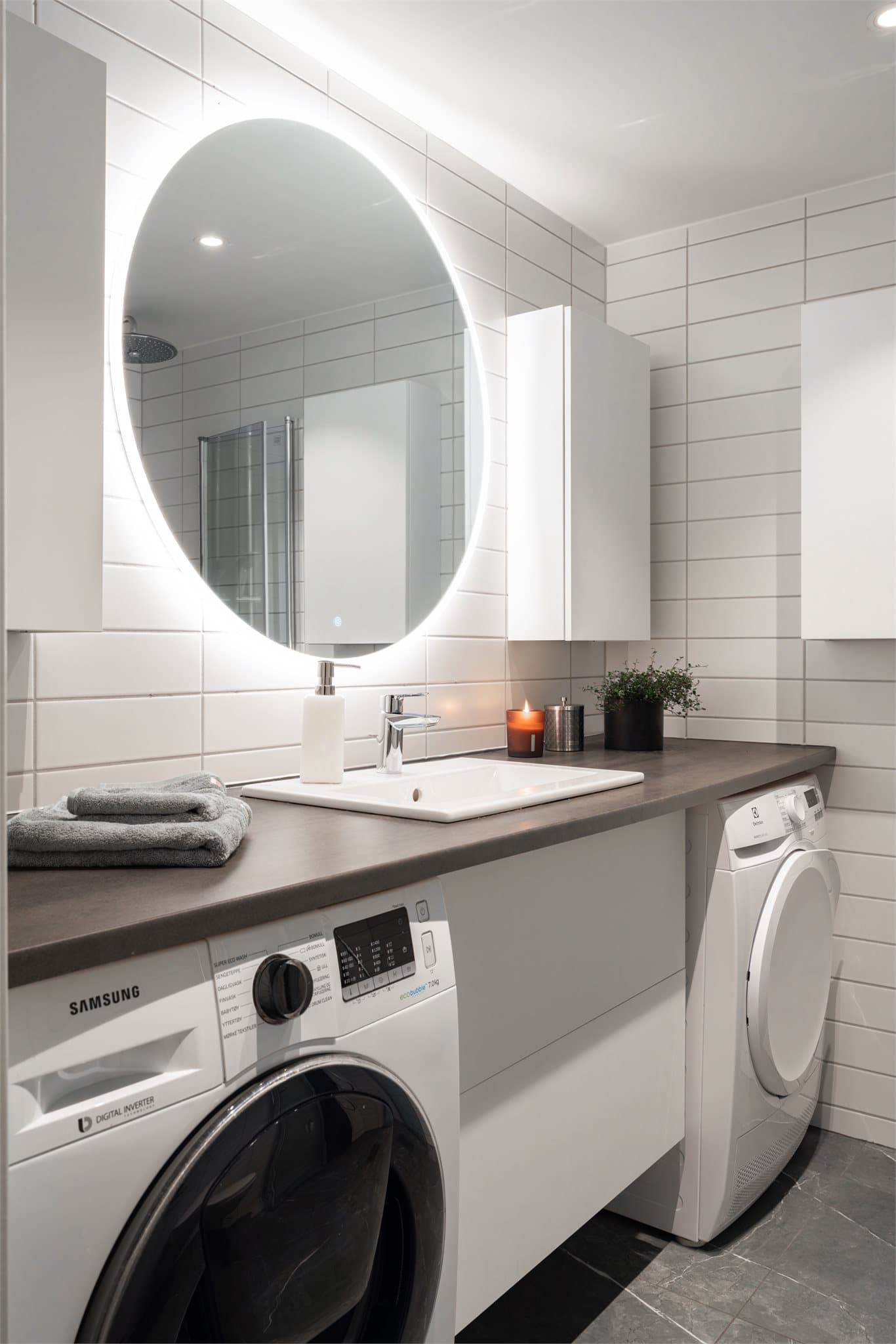 Innredningen består av heldekkende benkeplate med servant, underskap og god oppbevaringsplass, opplegg for vaskemaskin og tørketrommel og stort speil med belysning.