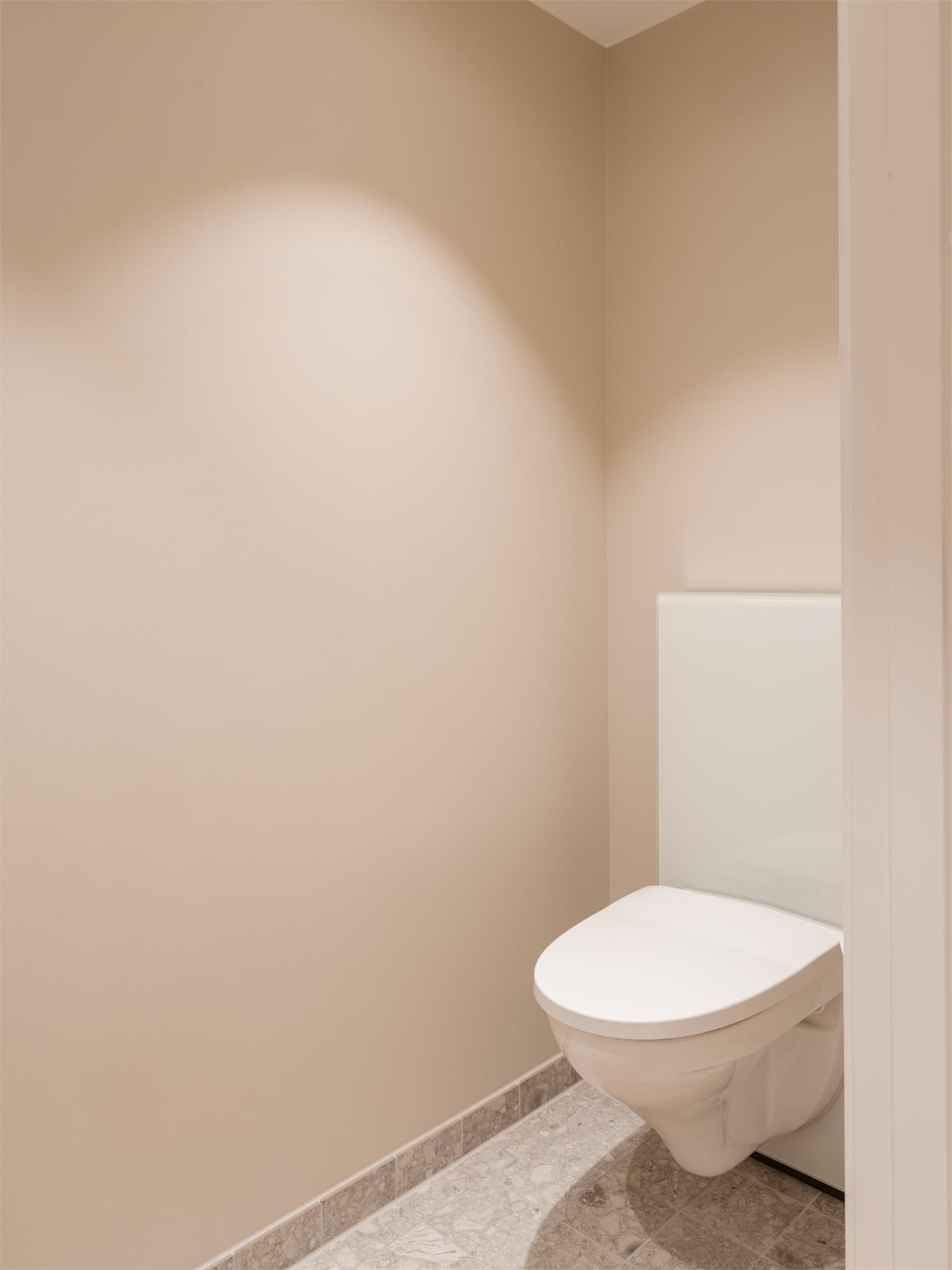 Toalettrommet er utstyrt med vegghengt toalett og fliser på gulvet.