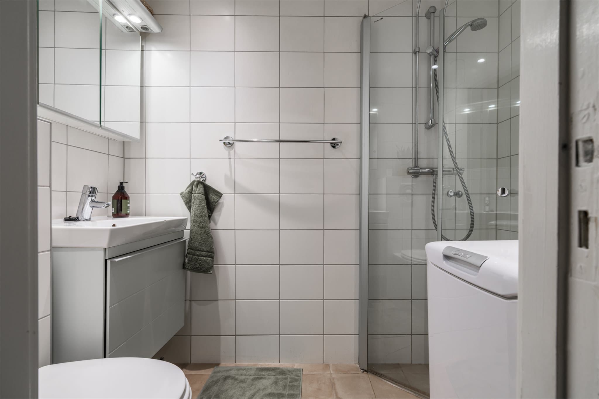 Flislagt bad med vegghengt toalett, dusjhjørne og opplegg for vaskemaskin.