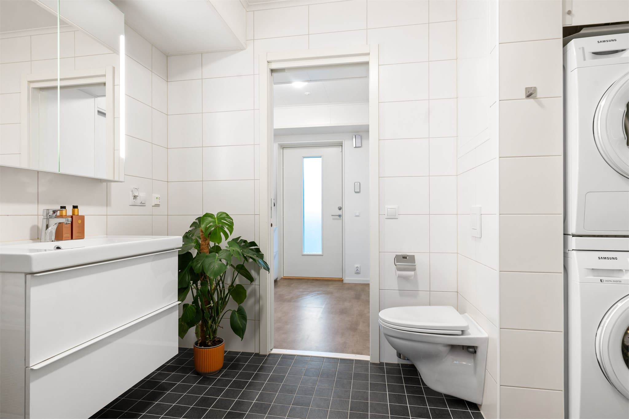 Badet er innredet med helservant på skuffeseksjon, speilskap, dusjhjørne og vegghengt toalett.